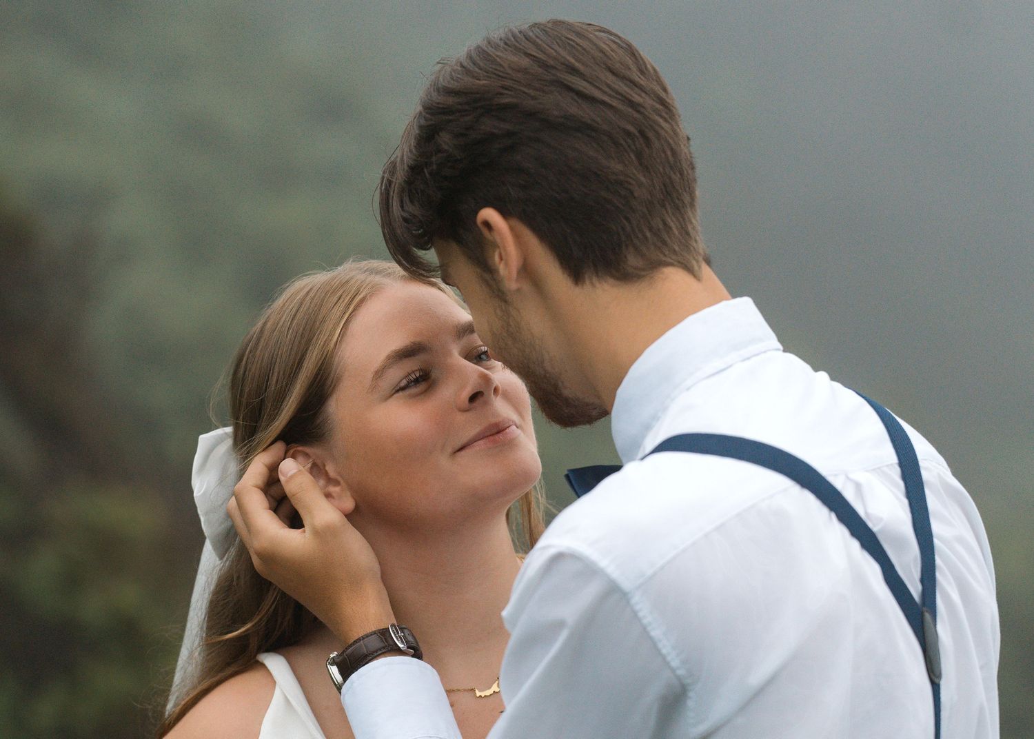 A romantic couple embraces closely against a backdrop of misty mountains.
