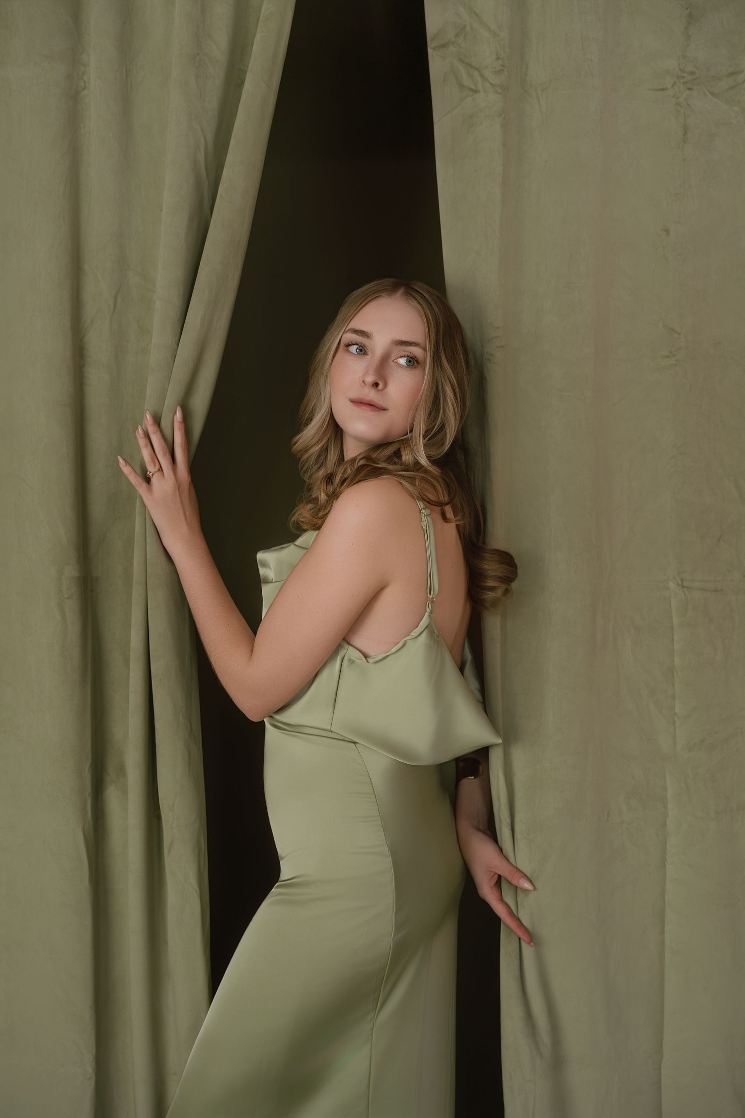 A series of artistic portrait photos showing someone in a sage green dress posing against beige curtains.