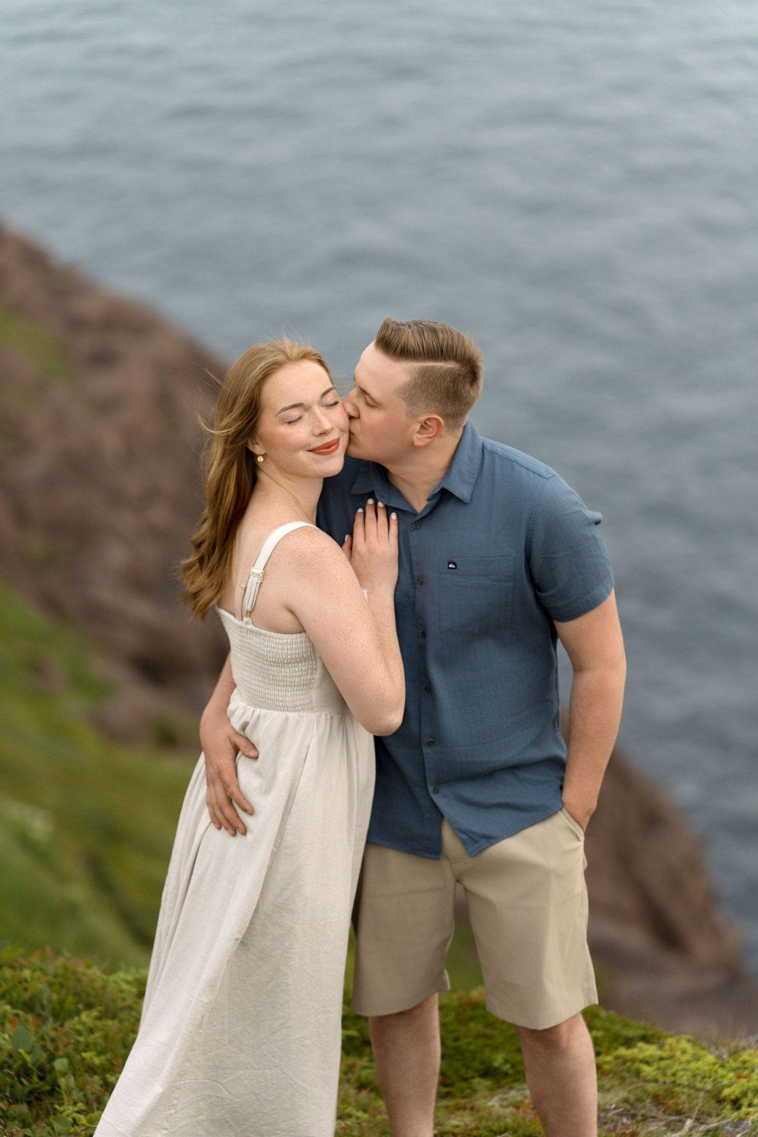 A romantic couple stands together by the ocean as they share a special moment on coastal cliffs.