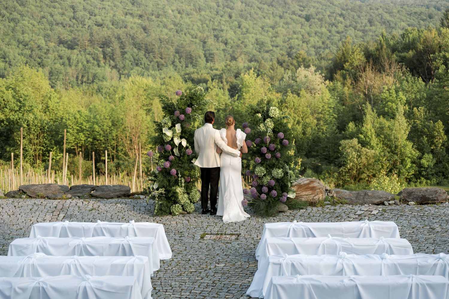 Wedding ceremony setup with white chairs and mountain views at an outdoor venue in lush green surroundings.