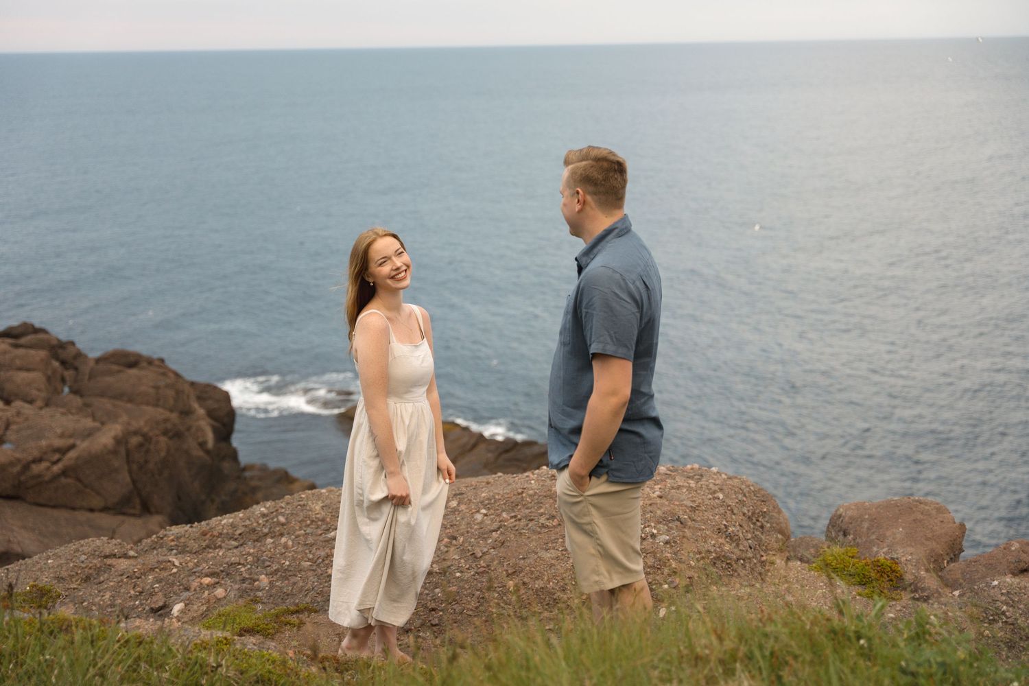 A couple shares a romantic moment on rocky coastal cliffs overlooking the ocean during a sunny afternoon.