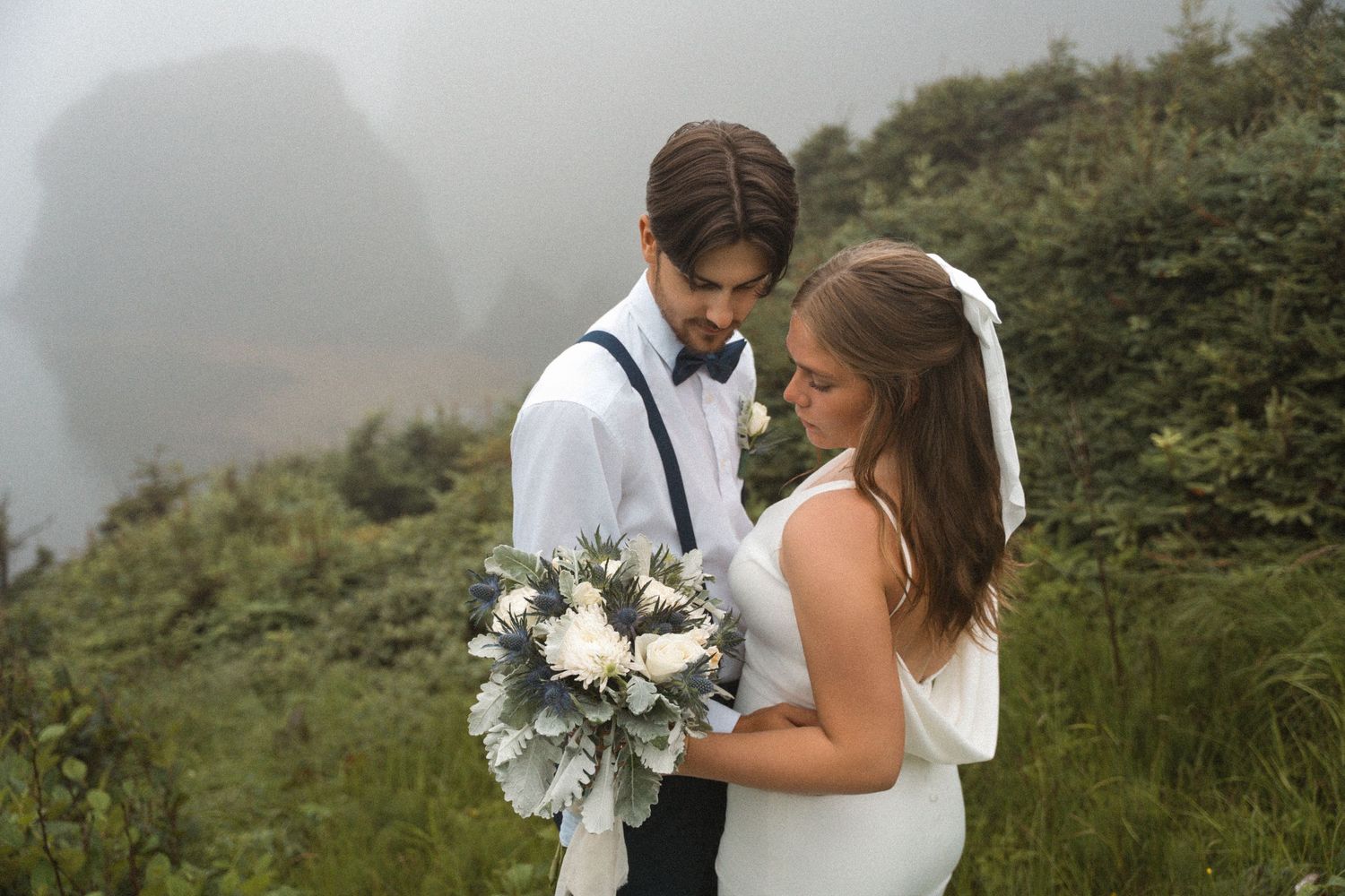Romantic moment between newlyweds along a dramatic coastal landscape.