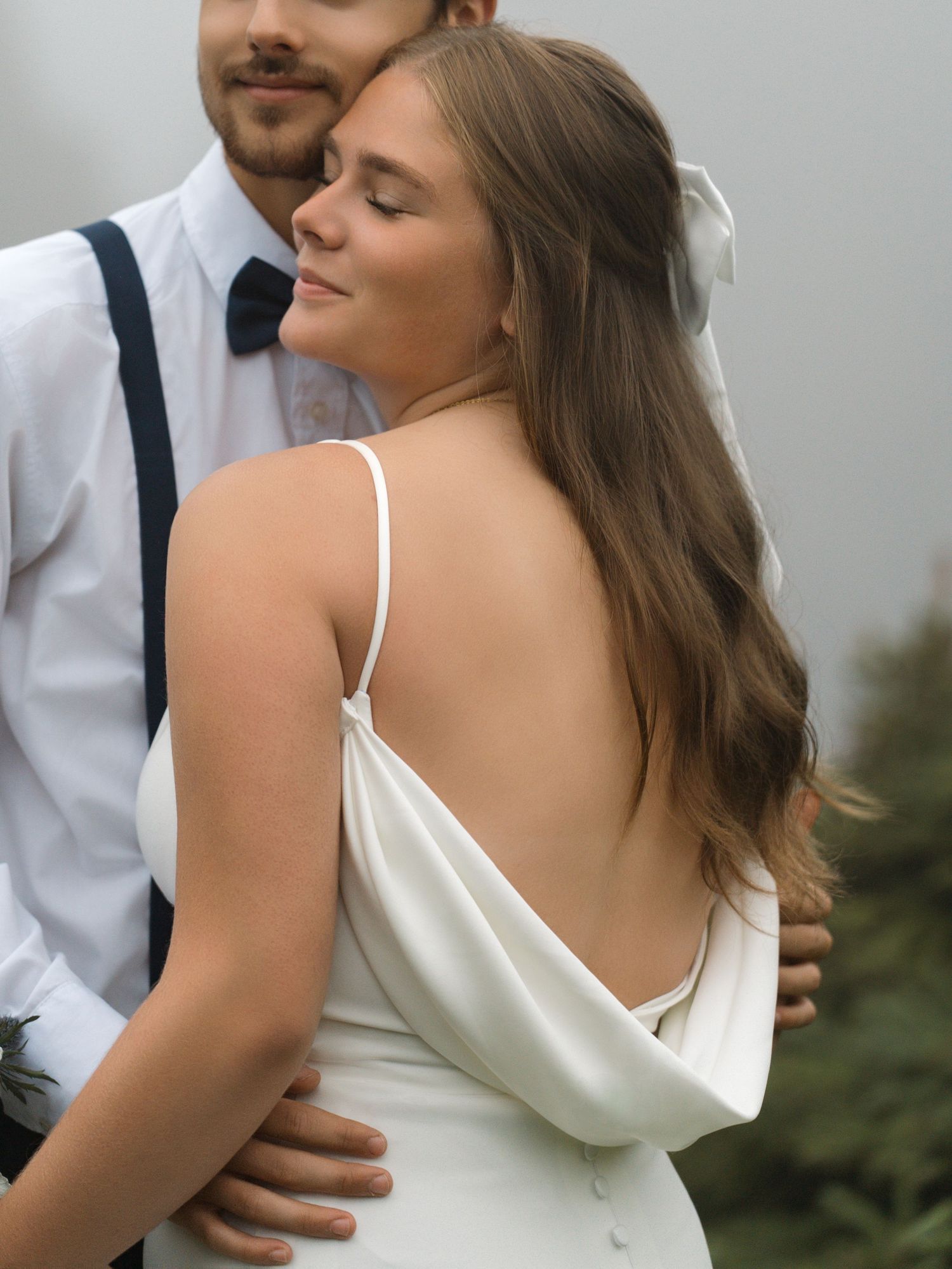 Romantic wedding couple embraces in garden wearing white dress and navy tie.
