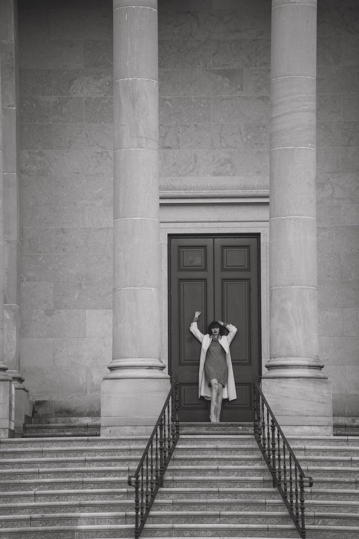 Black and white photo of person in dress posing between grand columns on stone steps.