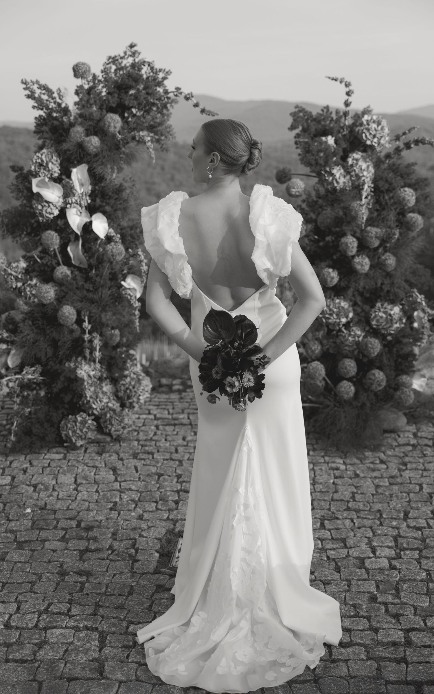 Black and white photos of a bride in a white wedding dress holding a floral bouquet against a stone wall backdrop.