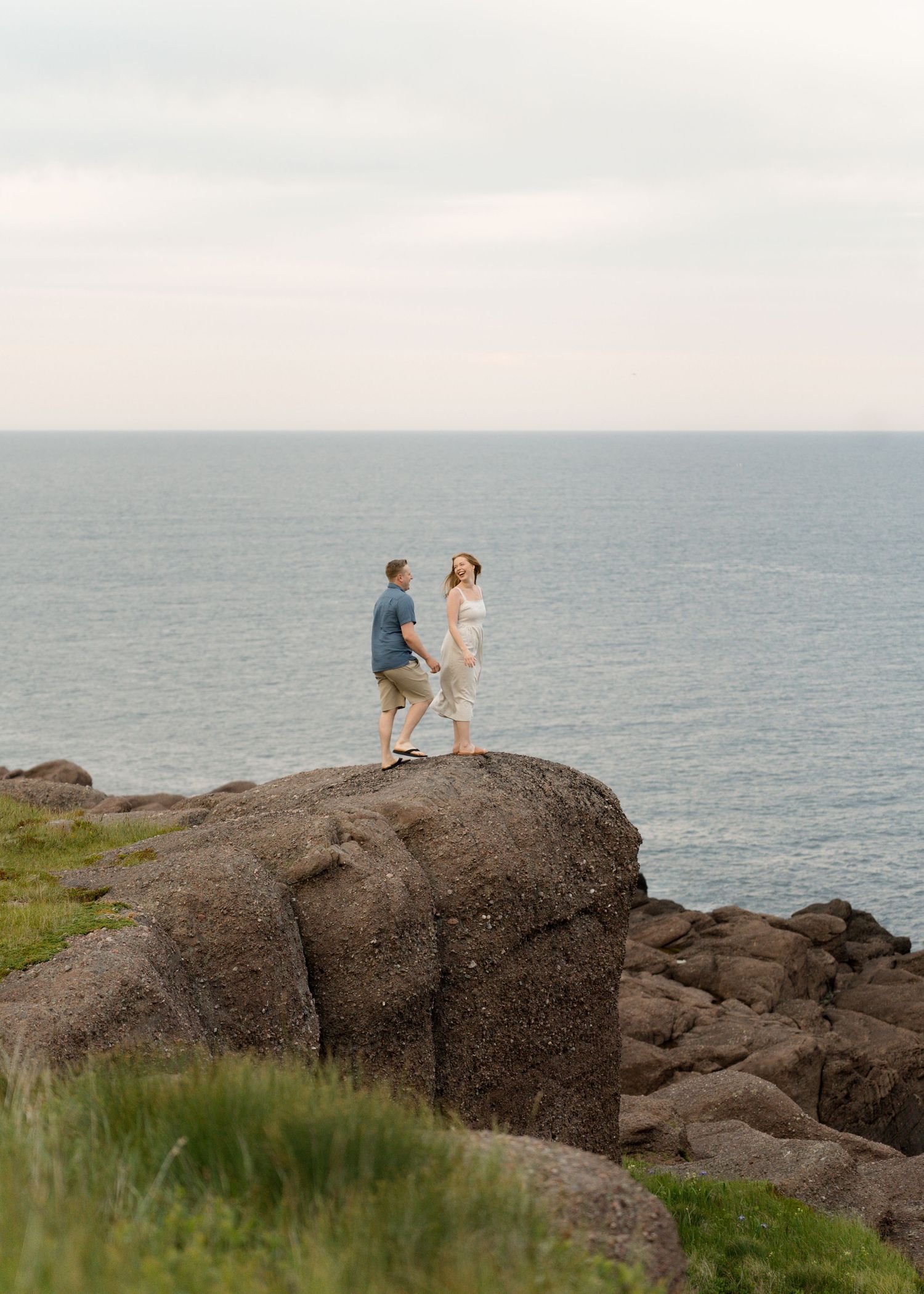 A couple shares an intimate moment on rugged oceanside rocks with waves and horizon in the background.