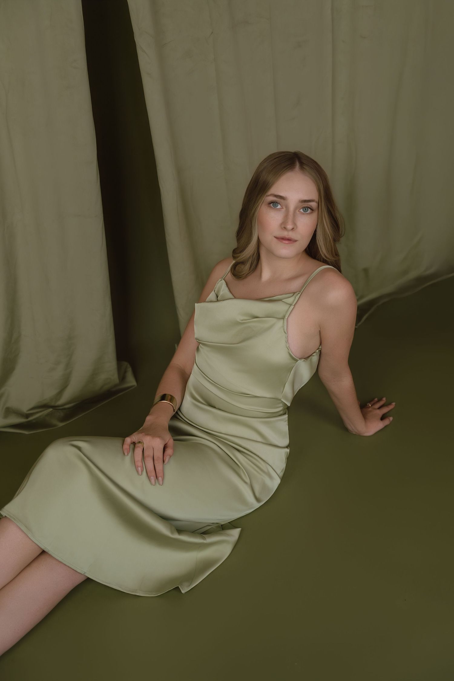 A series of moody portraits showing a person in a light sage green slip dress against a dark olive backdrop.
