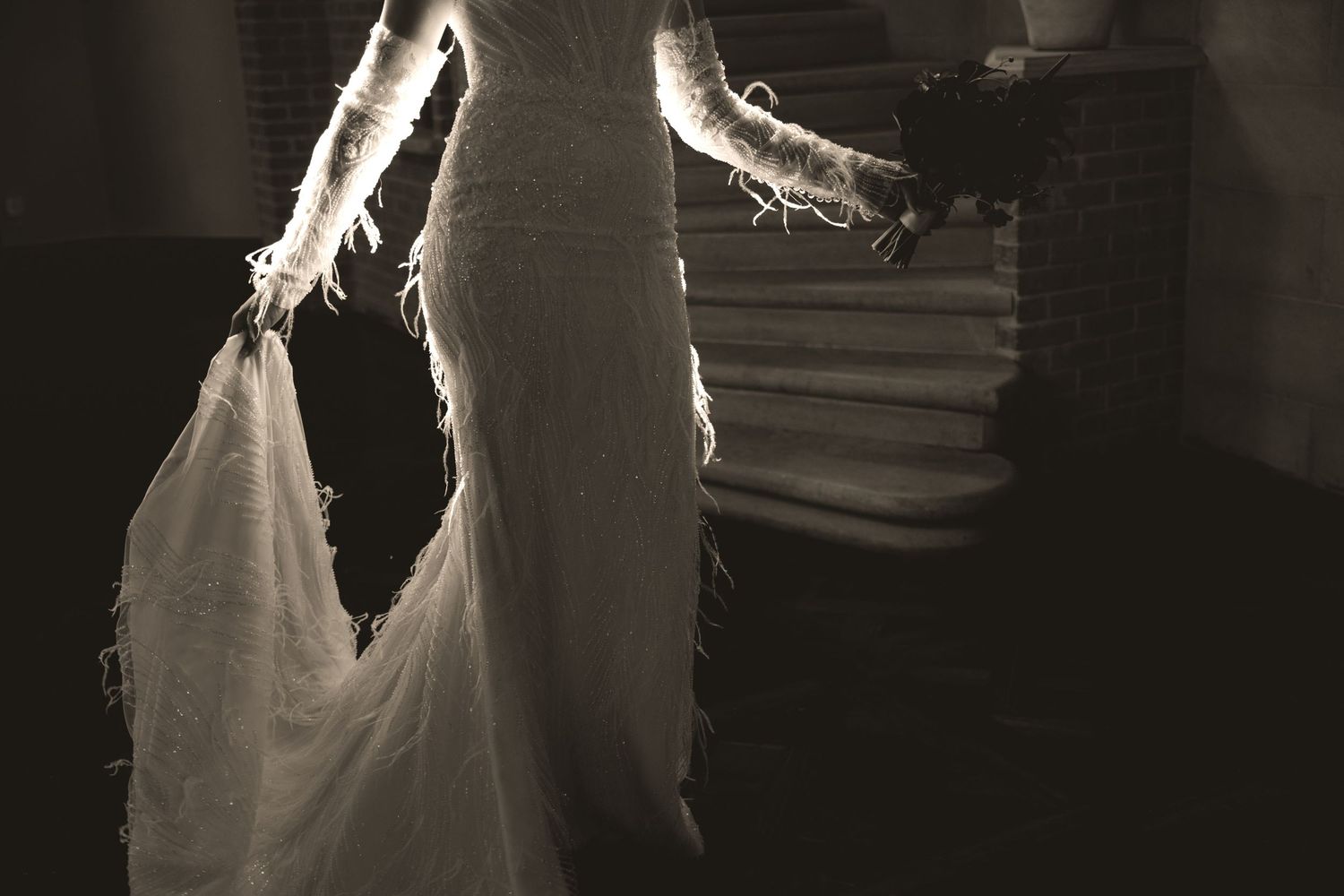 A bride in a flowing white wedding gown poses in an elegant interior setting with dramatic lighting.