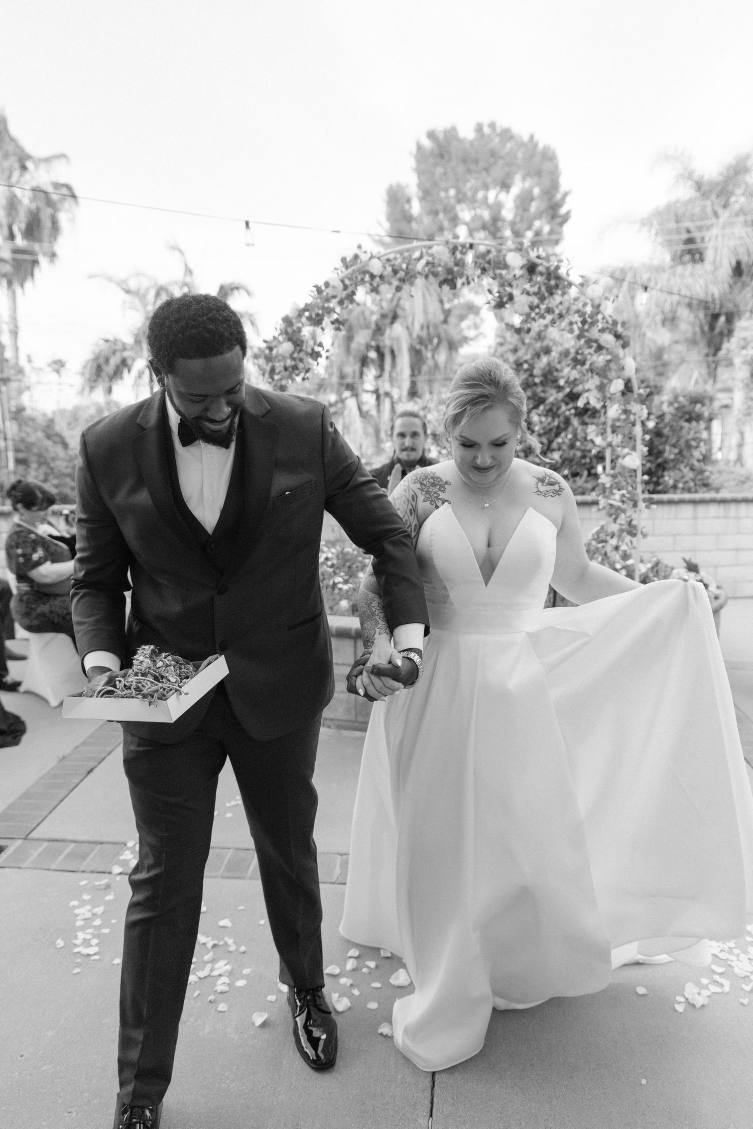 Newlyweds laughing while gathering dress fabric during outdoor wedding photos.