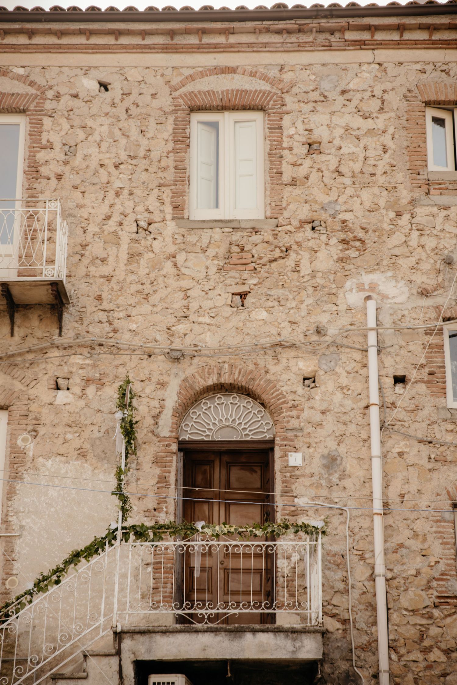 Stone wall facade of rustic Mediterranean building with arched doorways and small windows framed by decorative ironwork.