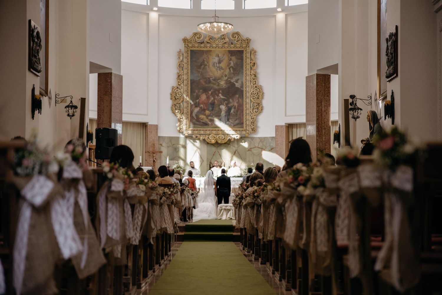 Interior view of a traditional church with wooden pews and ornate decorations during what appears to be a wedding ceremony.