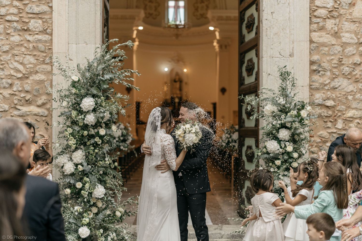 Wedding reception in a stone-walled venue decorated with lush white floral arrangements.