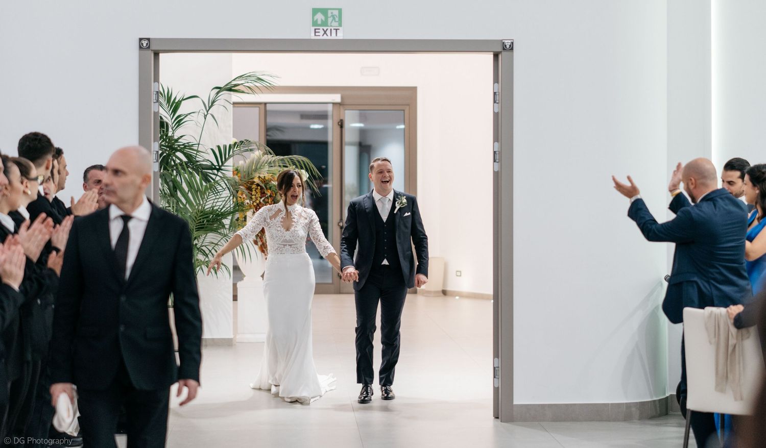 A group of formally dressed people walking through a modern white hallway with a doorway.