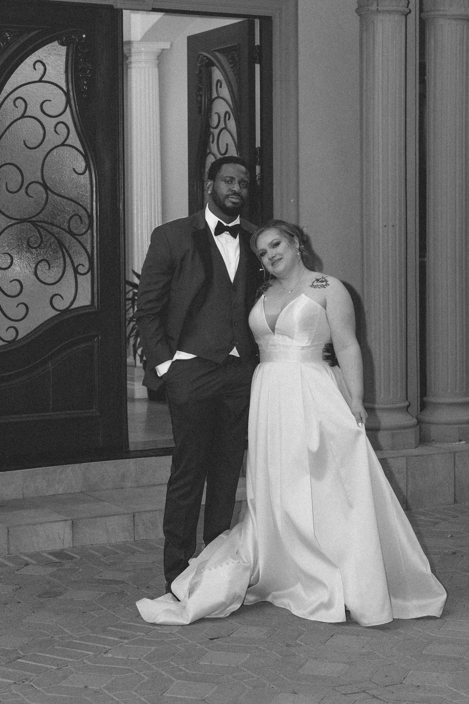 A wedding couple poses in front of an ornate door in classic black and white photography.