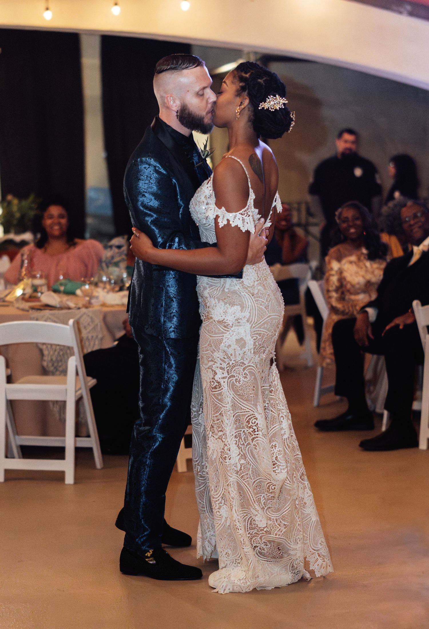 A romantic first dance between newlyweds at their wedding reception with guests watching in the background.