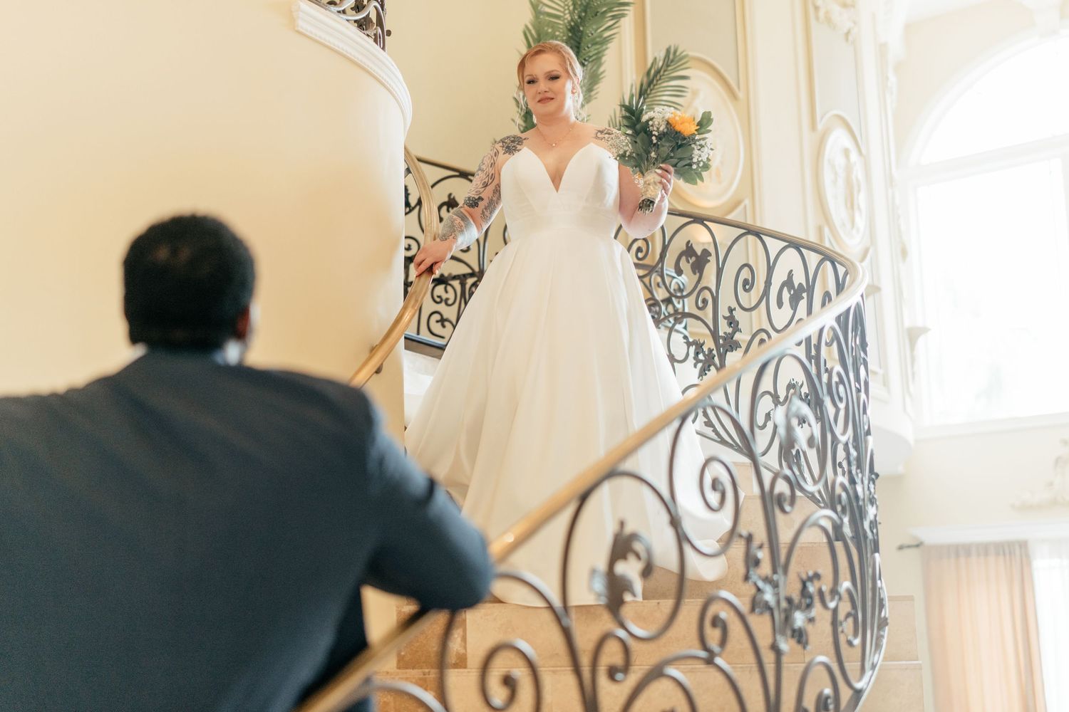 Wedding couple playfully interacting on grand staircase with decorative railings.
