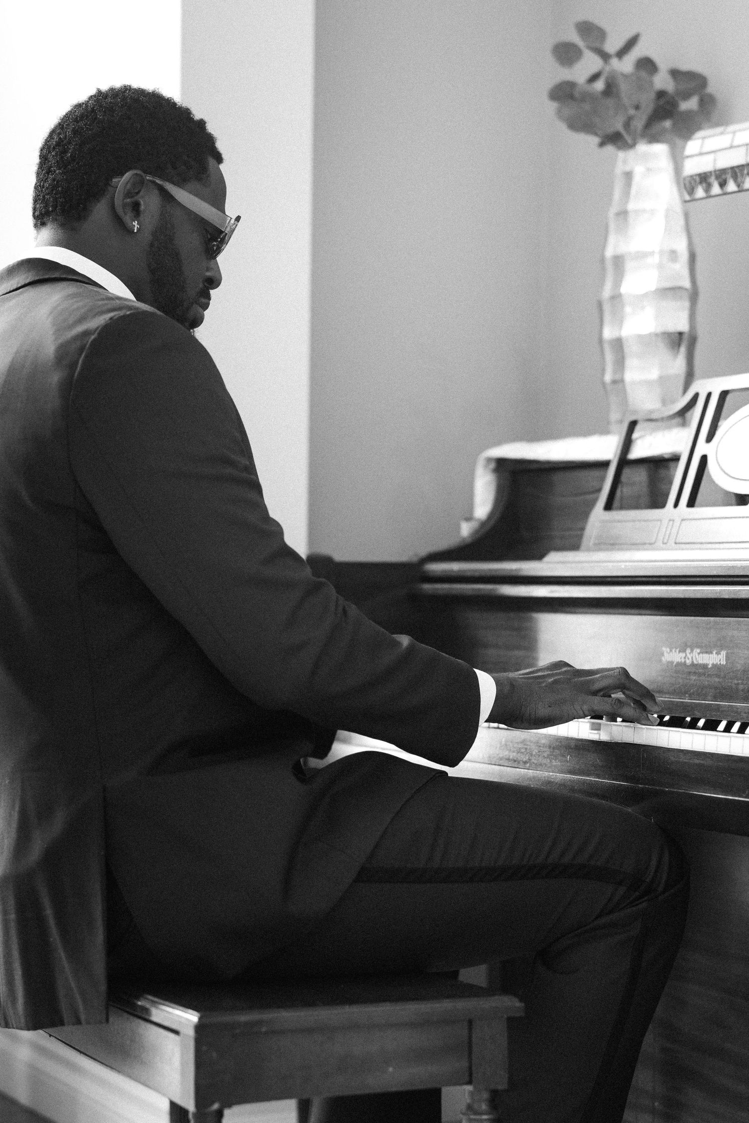 A person in formal attire seated at a piano in an elegant room.