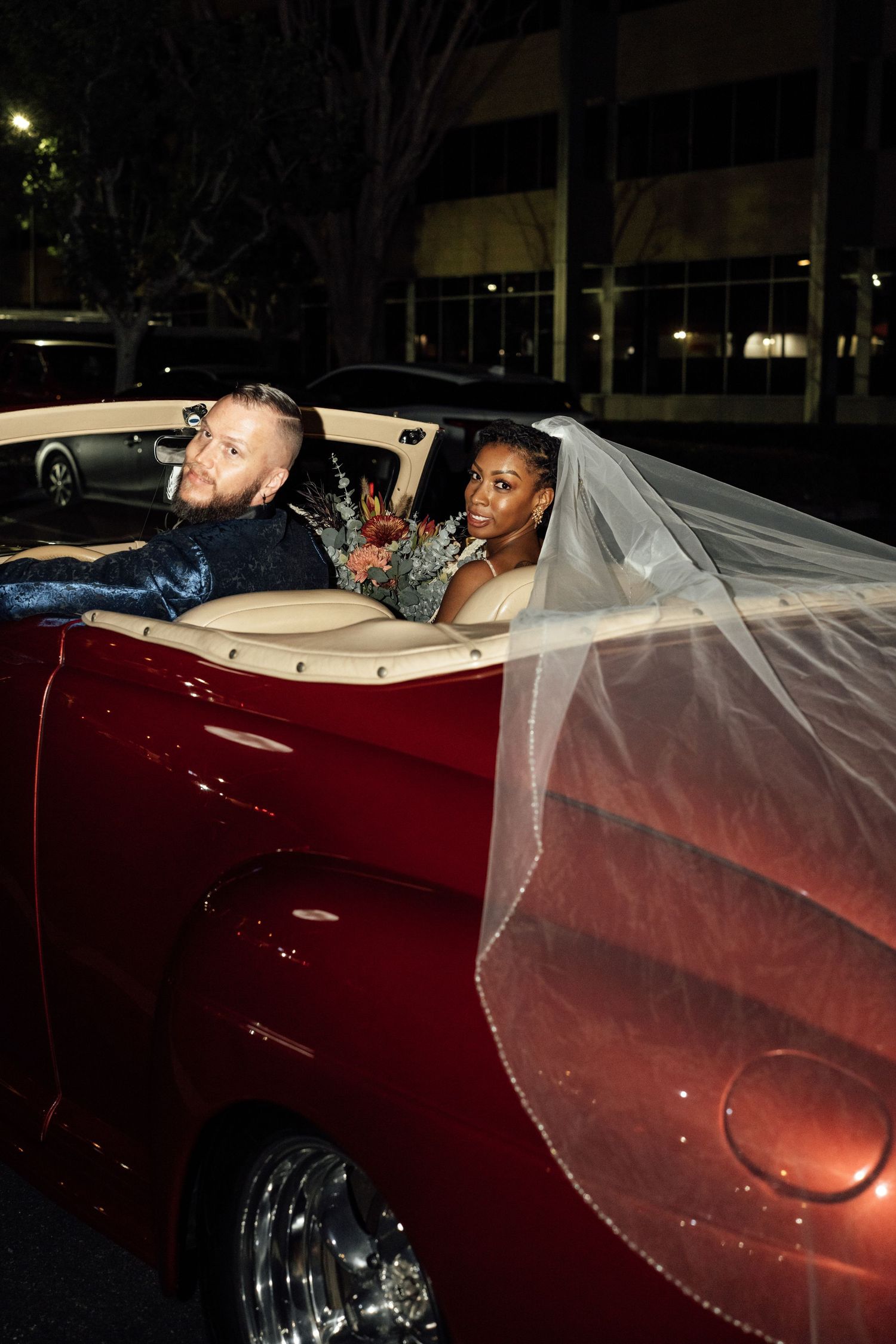 A red vintage convertible car with flowing white fabric visible in a nighttime setting.