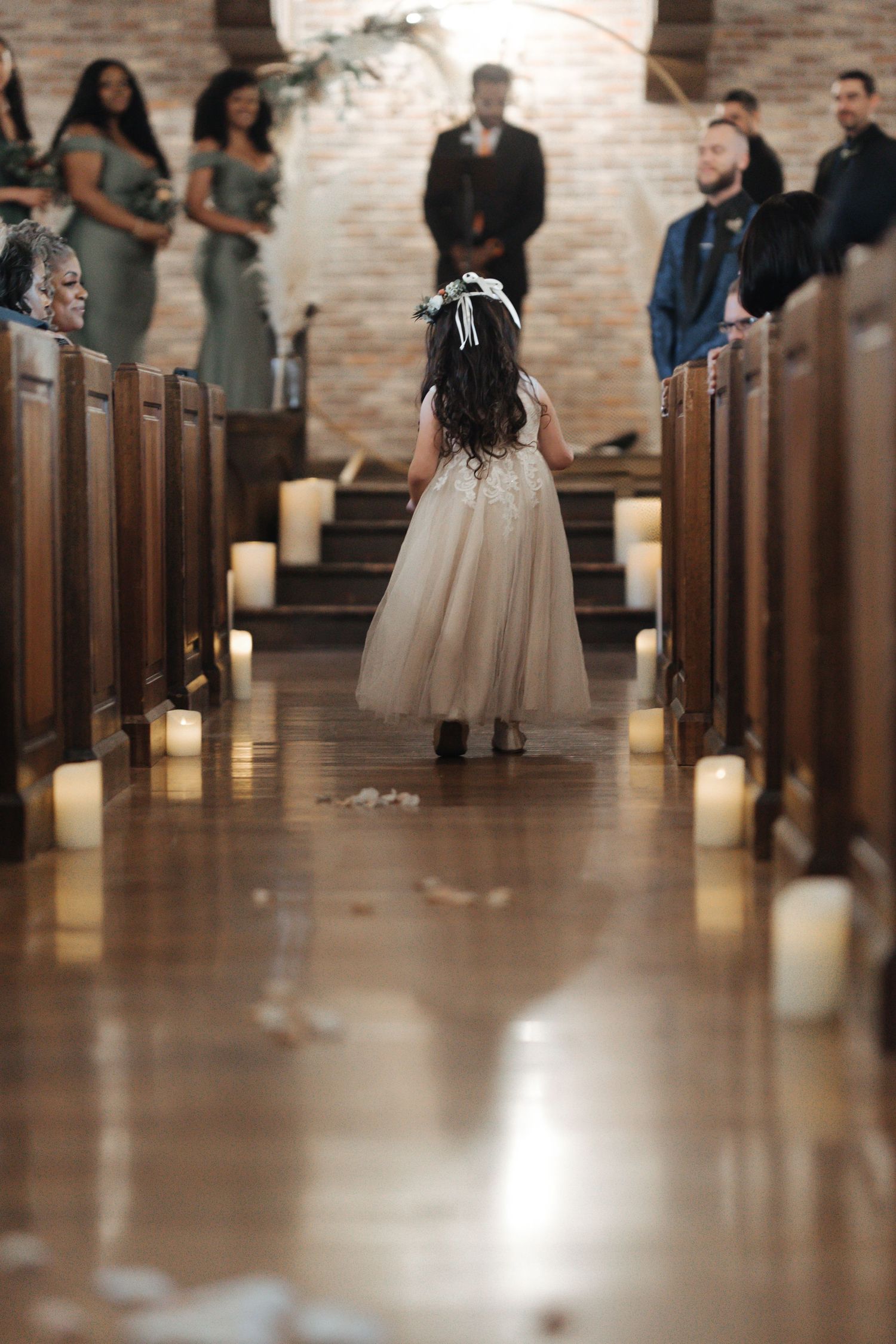 A candlelit church aisle lined with wooden pews and glowing candles as a bride walks down during a ceremony.