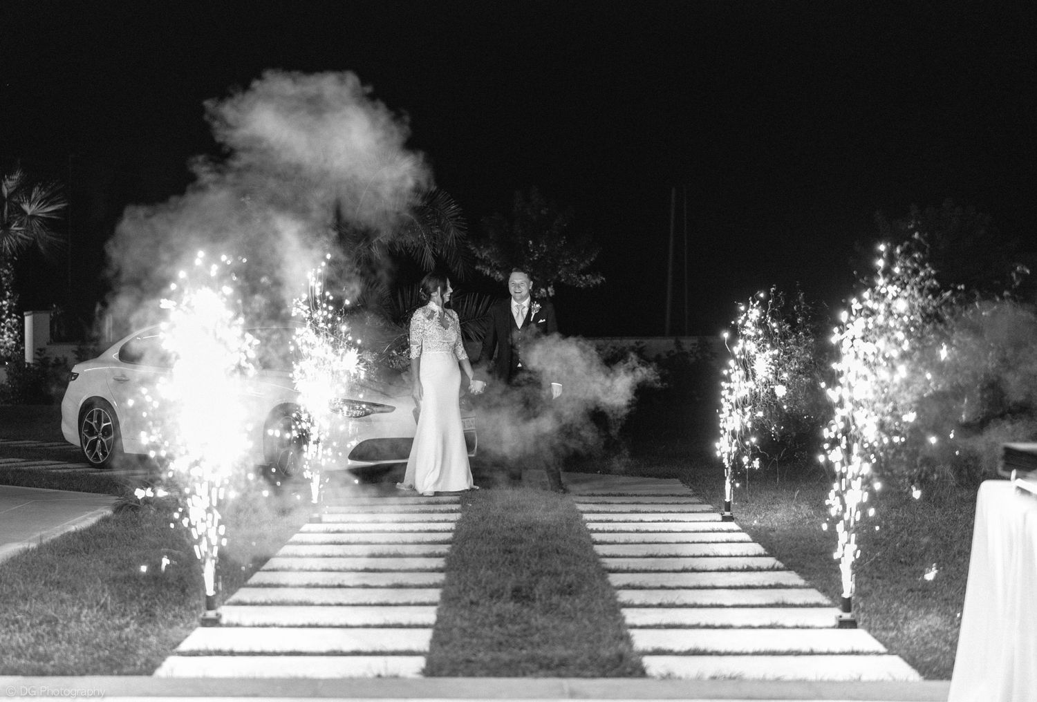 A dramatic black and white wedding exit with sparklers creating a illuminated pathway.