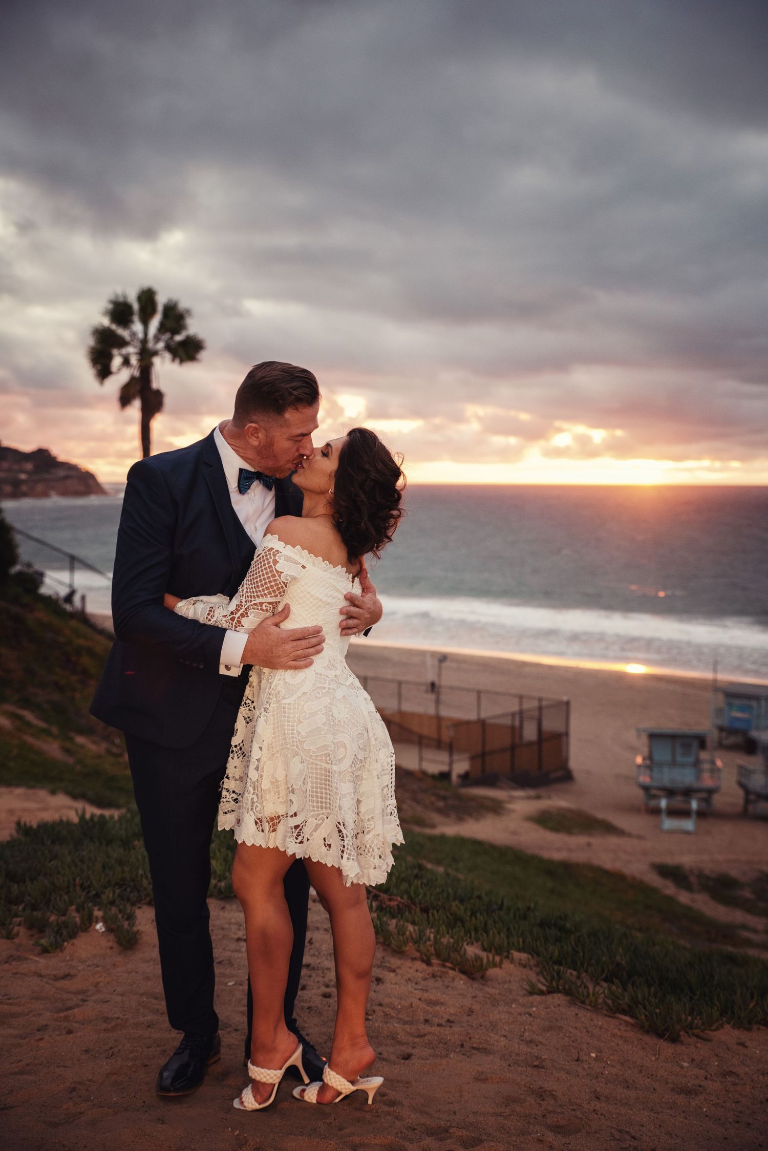 A romantic couple shares an intimate moment at sunset on a coastal cliff overlooking the ocean.