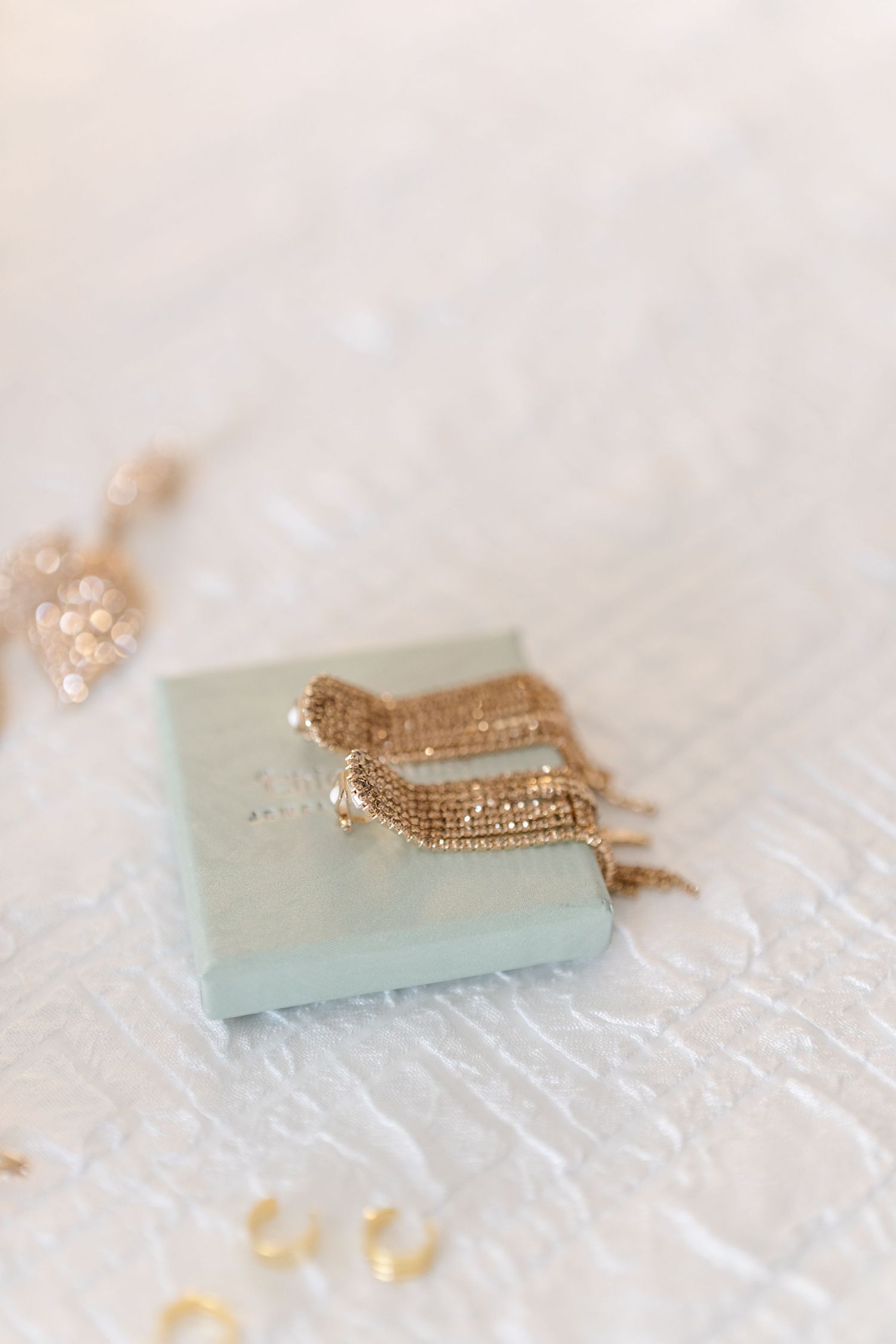 Delicate gold wedding jewelry displayed on pale blue surface.
