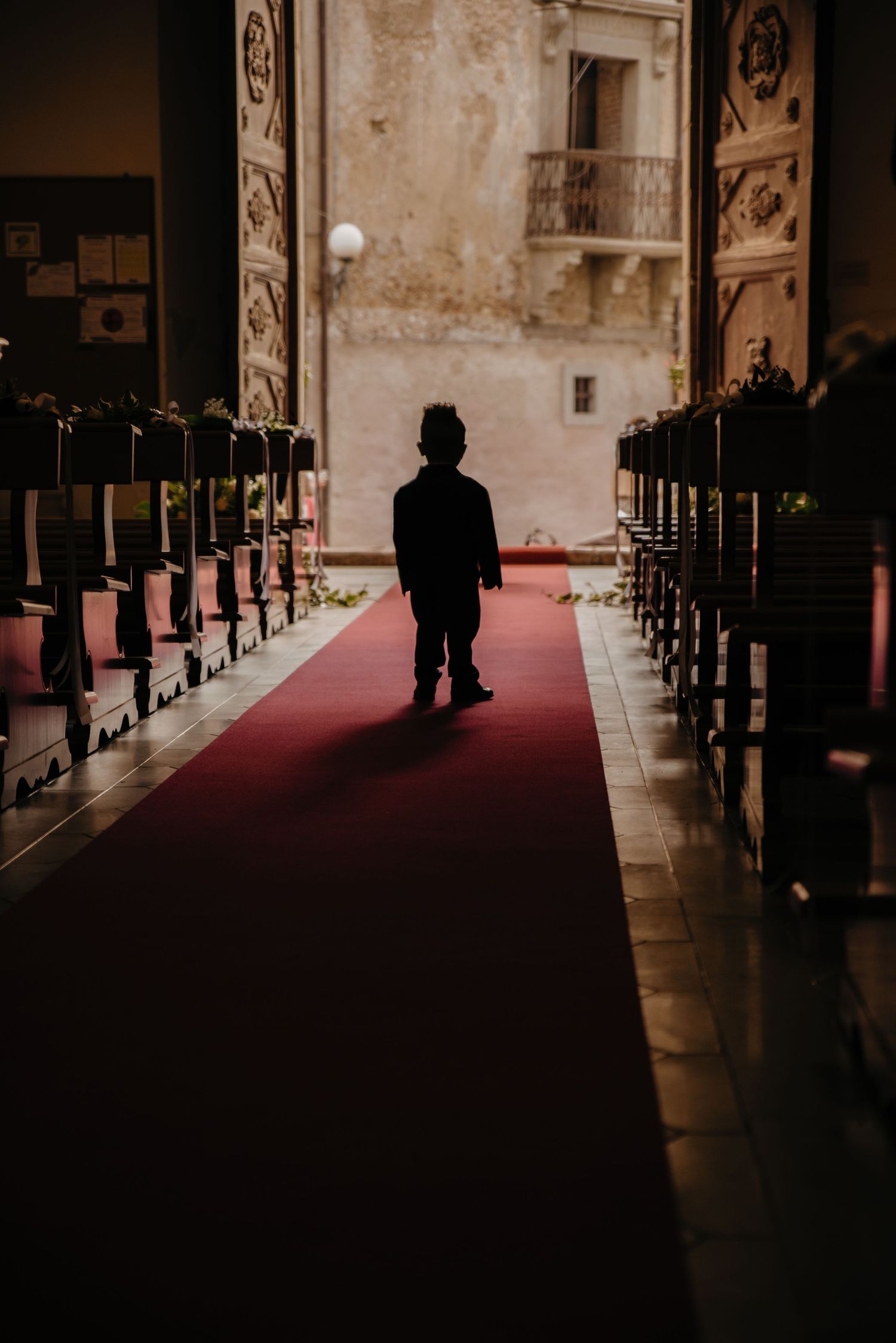 A silhouette walks down a dimly lit church aisle with red carpet and wooden pews creating a dramatic perspective.