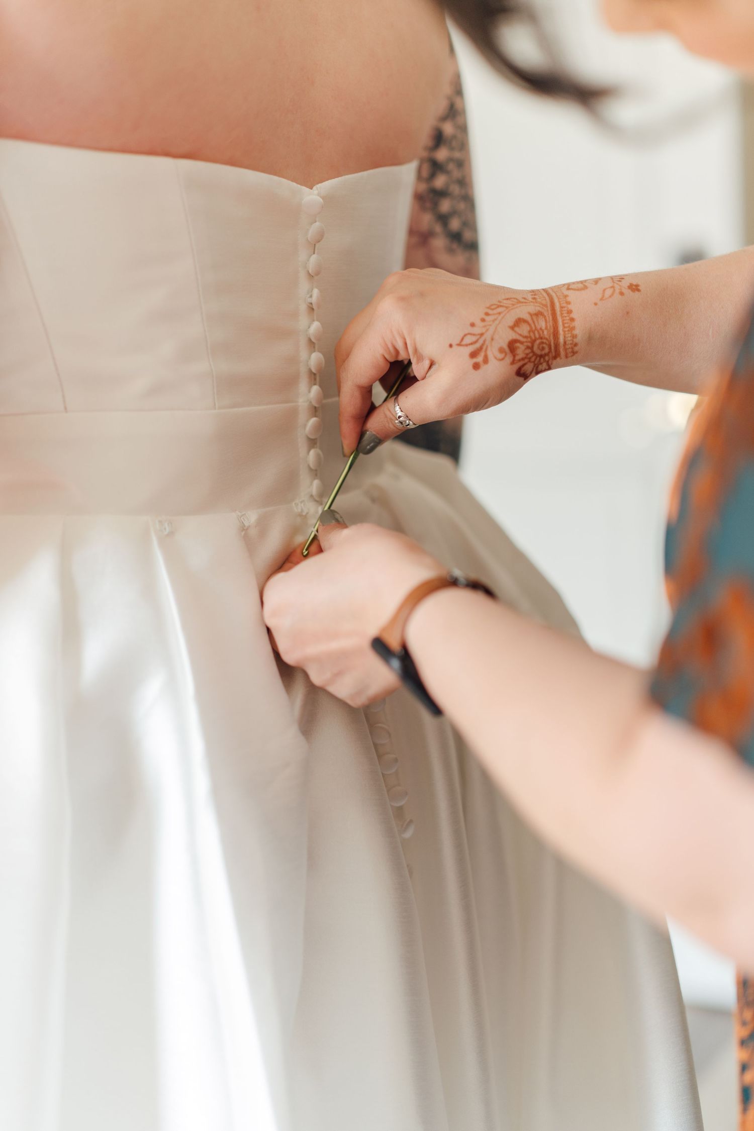 Detailed view of hands buttoning up the back of a white wedding dress.