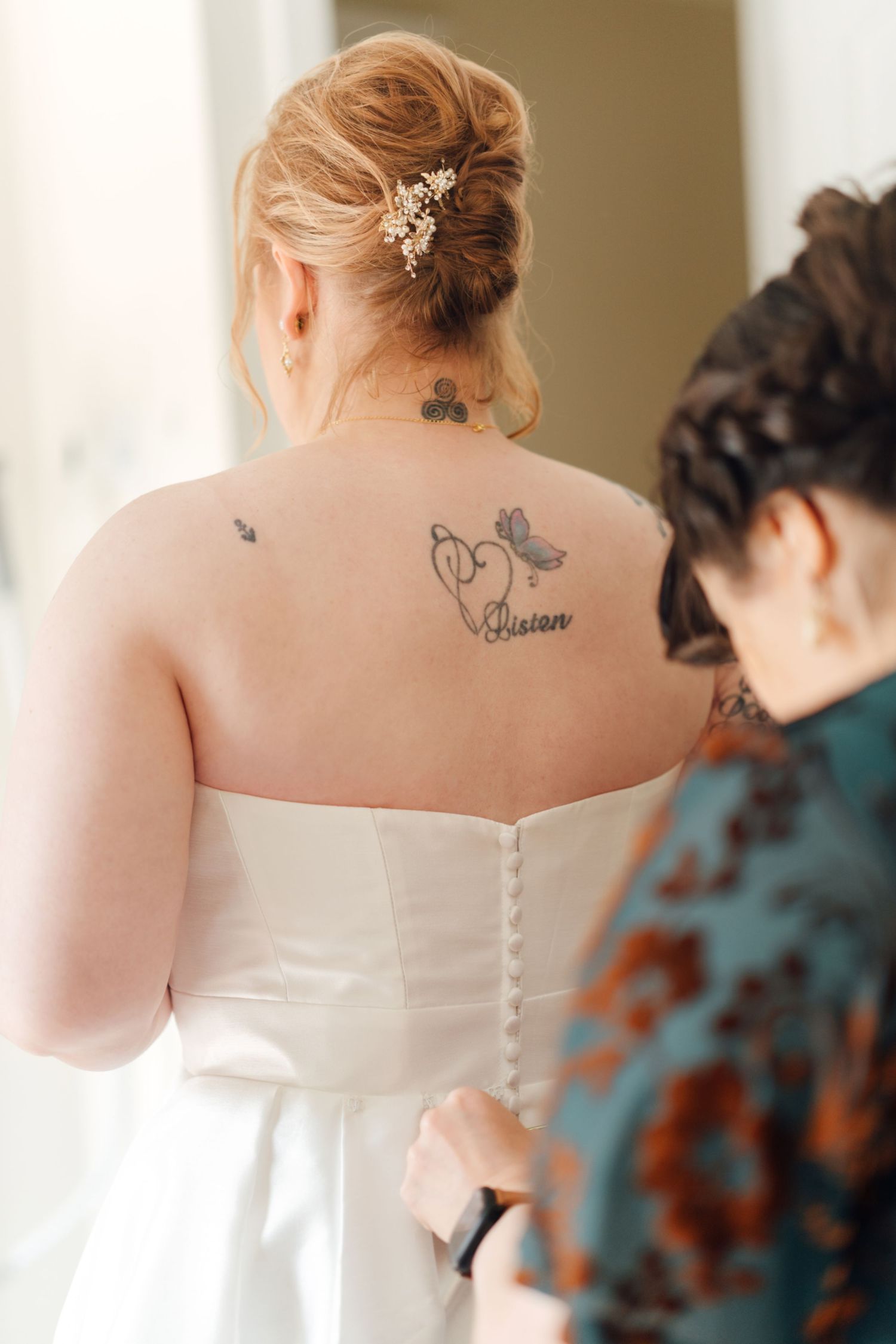 Back view of a white wedding dress showing delicate button details and tattoo artwork.