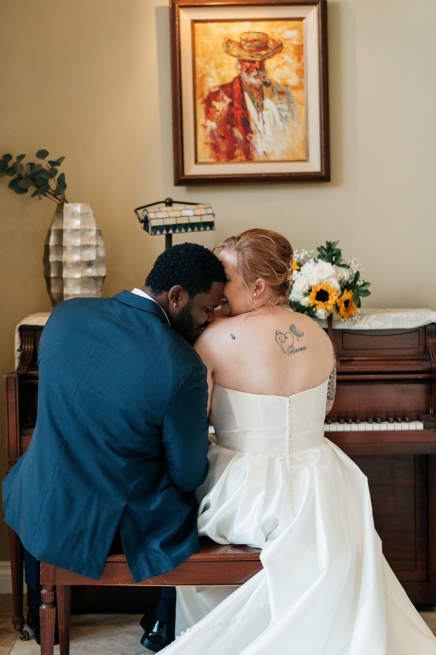 Wedding couple sharing an intimate moment at a piano with sunflowers in an elegant room.