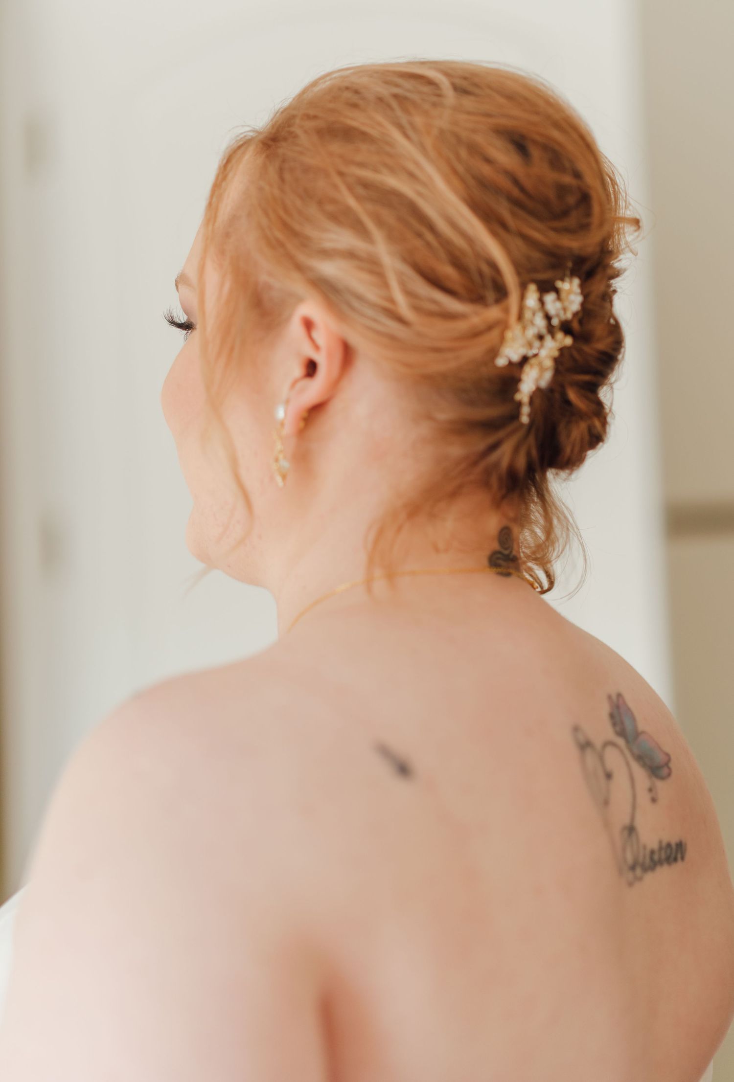 Side view of an elegant bridal hairstyle with delicate hair accessories and visible tattoo.