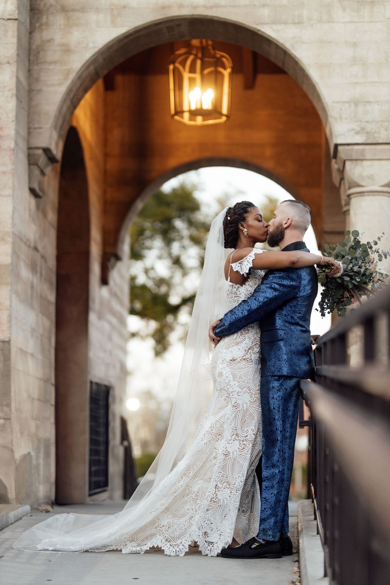 A romantic wedding couple embraces under a stone archway at sunset with beautiful architectural details.