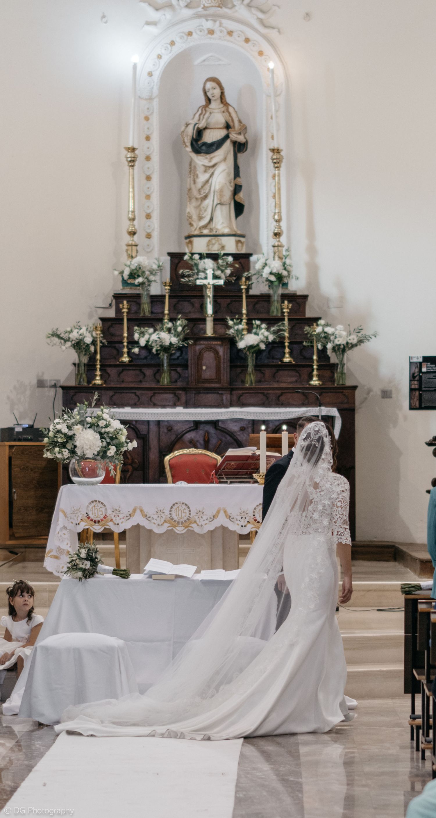 Four white wedding dresses laid out on church steps with religious statues and candles in the background.