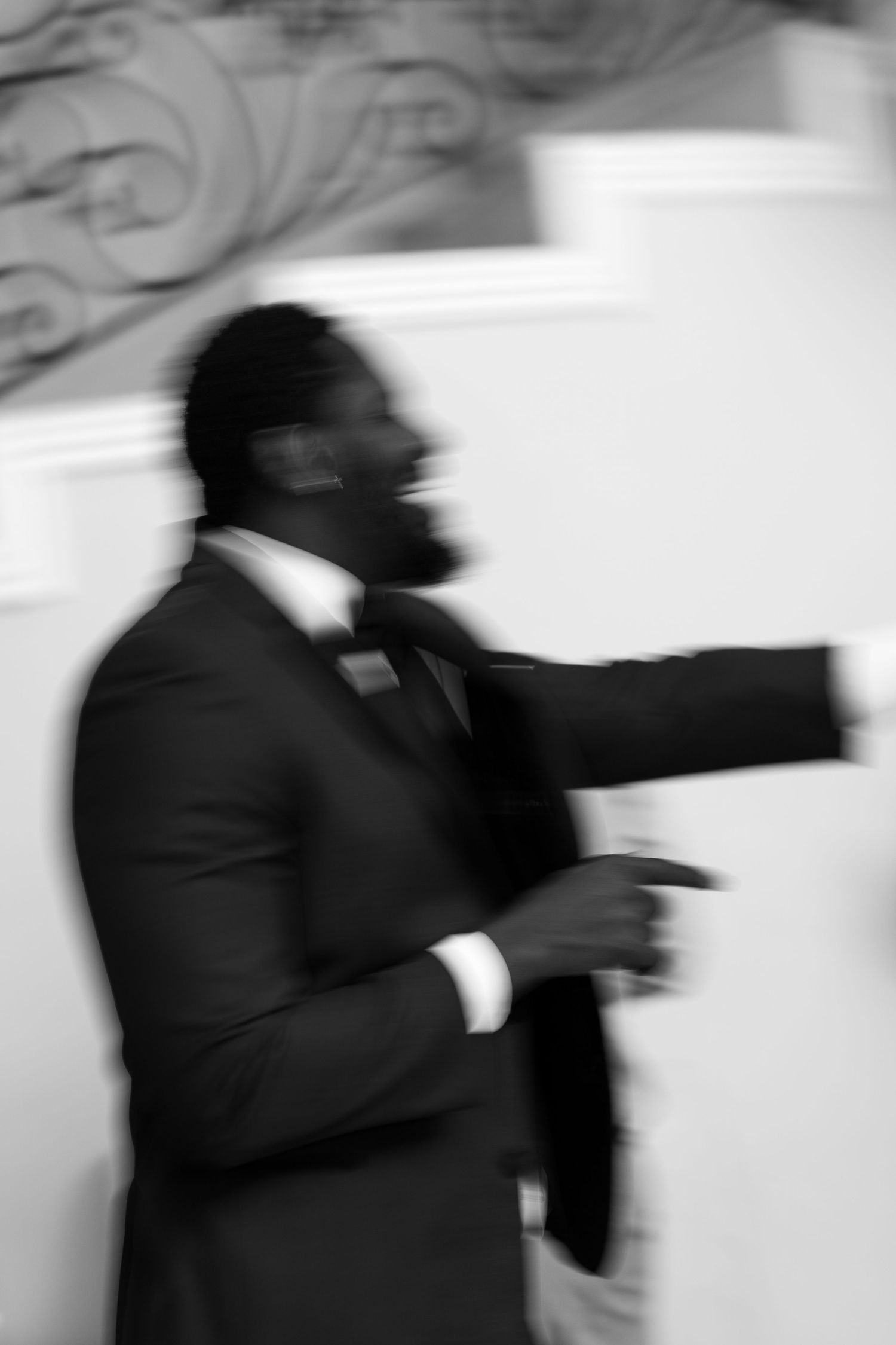 A motion-blurred black and white photo of a person in a suit gesturing during a speech.