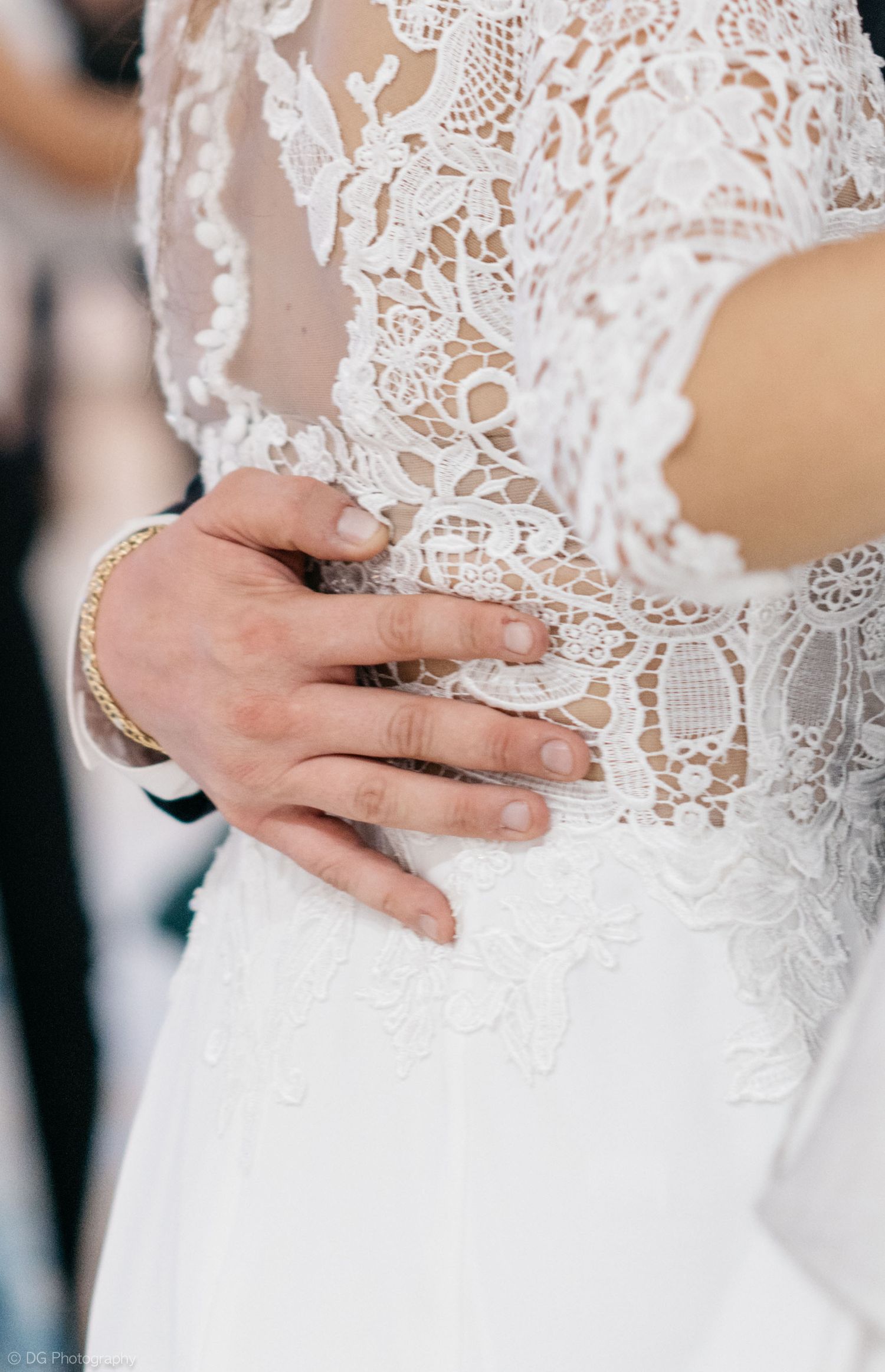 Close-up details of delicate white lace wedding dress bodice with hands gently touching the waist.