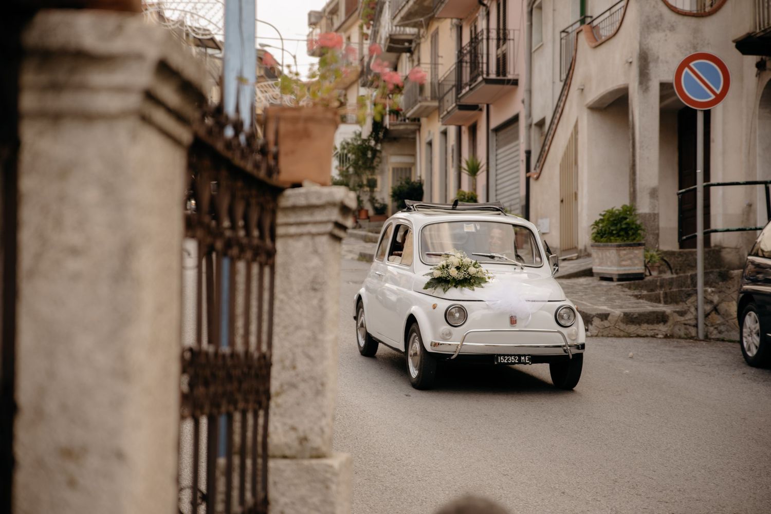Vintage white Volkswagen Beetle parked on a narrow cobblestone street in an old European town.