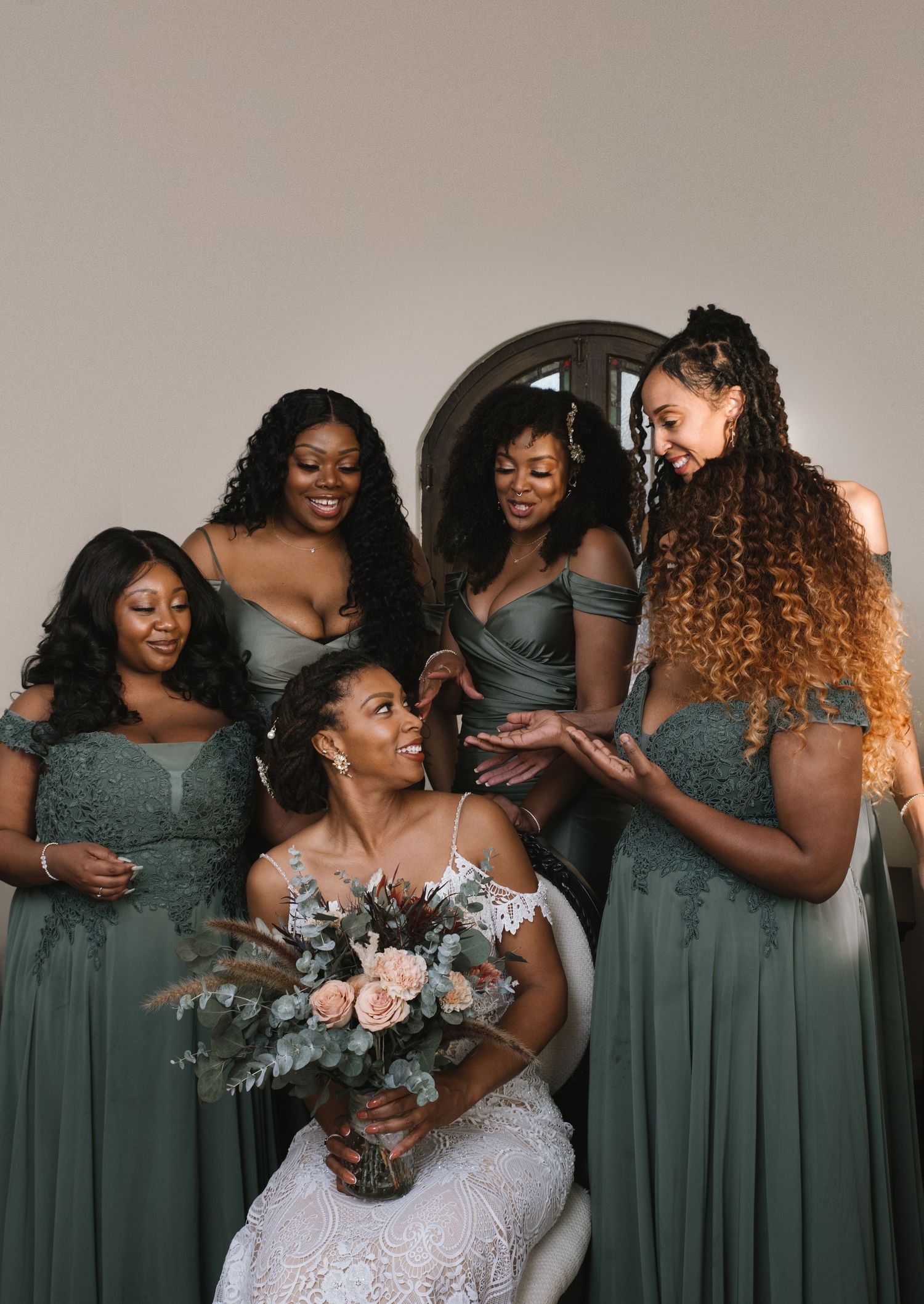 Bridesmaids in sage green dresses gather around a bride holding a beautiful blush and eucalyptus bouquet.
