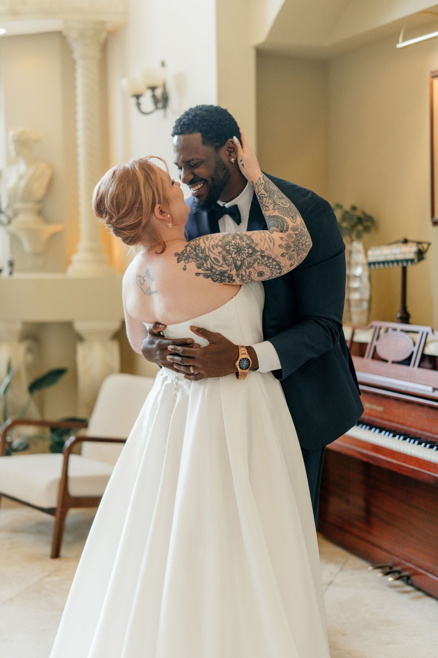 A romantic first look moment between newlyweds near a piano in a bright interior.