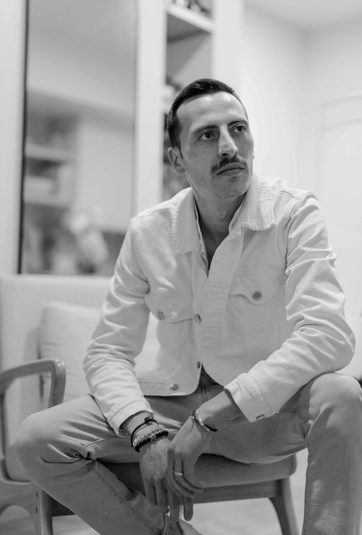 A black and white portrait of a person in a white jacket seated indoors.