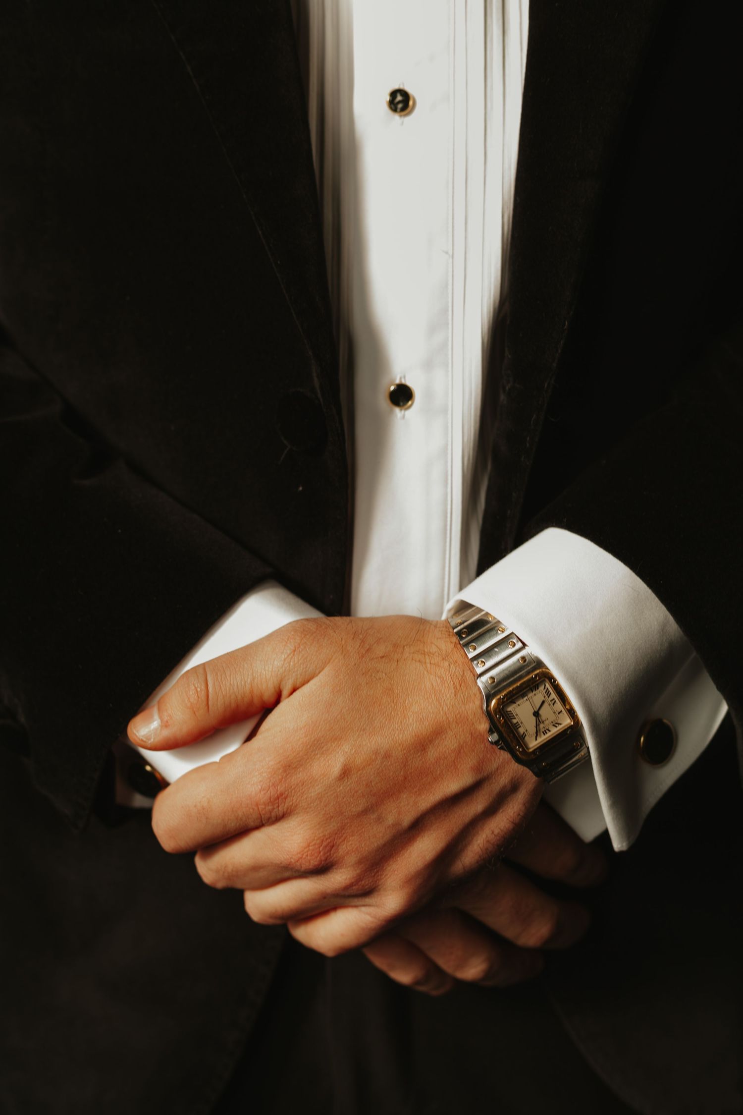 Close-up of formal attire showing black tuxedo sleeve with watch and cufflink.