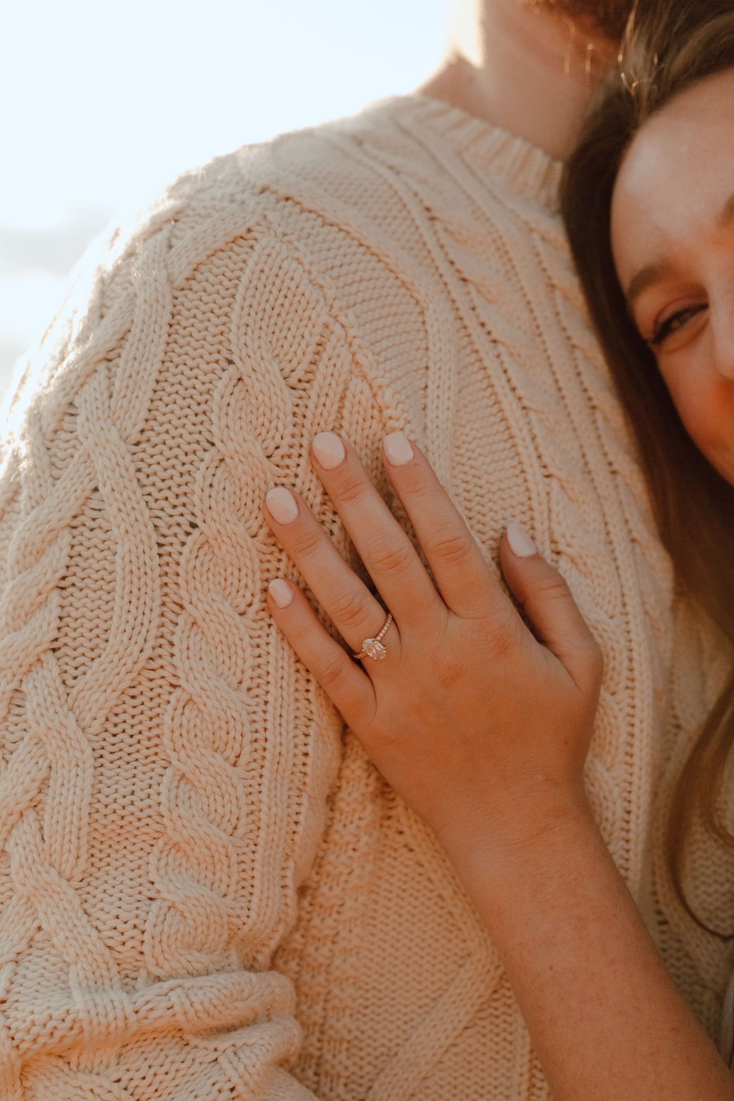 Close-up of an engagement ring on a hand resting against a cream cable knit sweater.