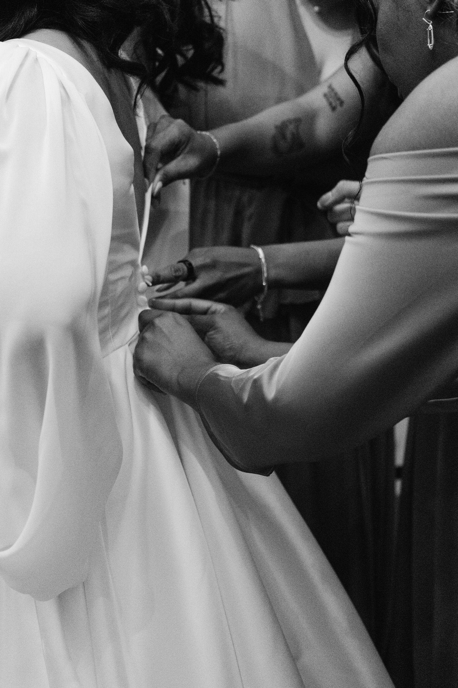 A series of black and white photos showing someone being helped into an elegant white wedding dress.