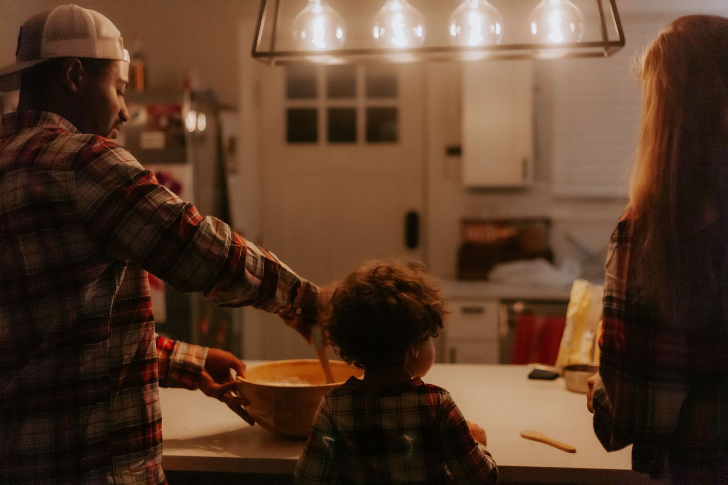 A family cooking together in a warmly lit kitchen during evening hours.