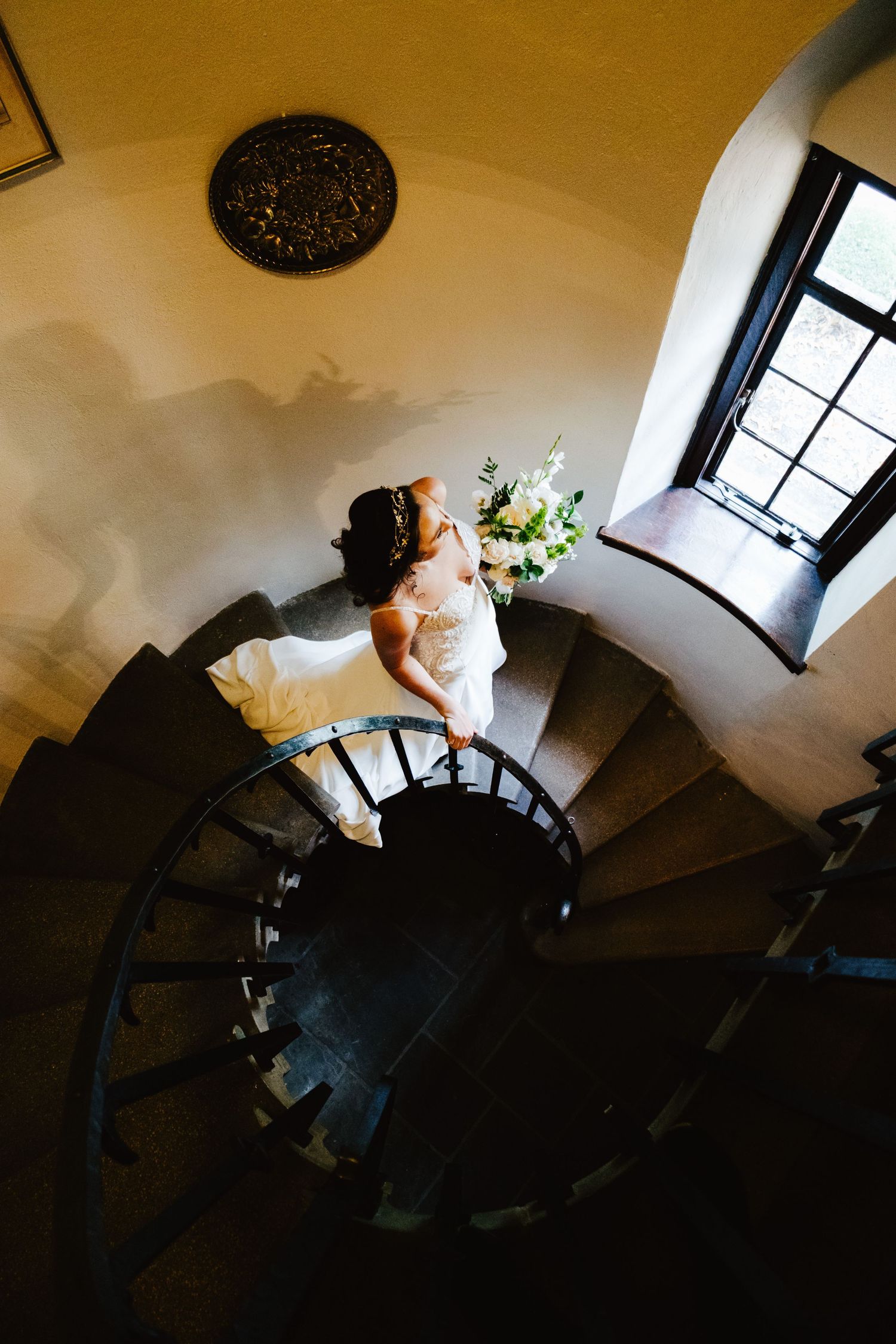 A spiral staircase sequence shows a person in white ascending the curved steps in dramatic lighting.