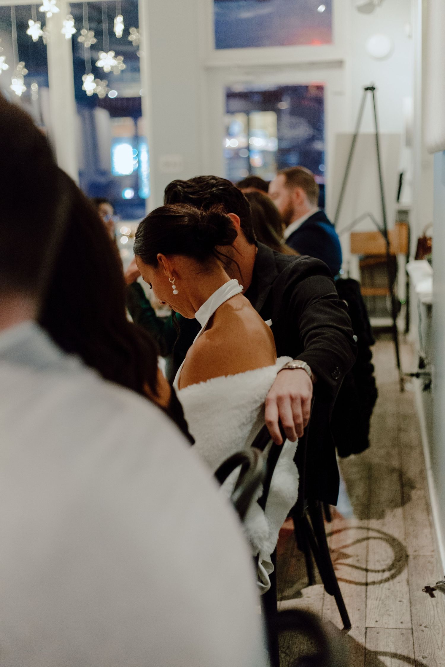 An intimate moment between newlyweds during their wedding reception with decorative lights in the background.