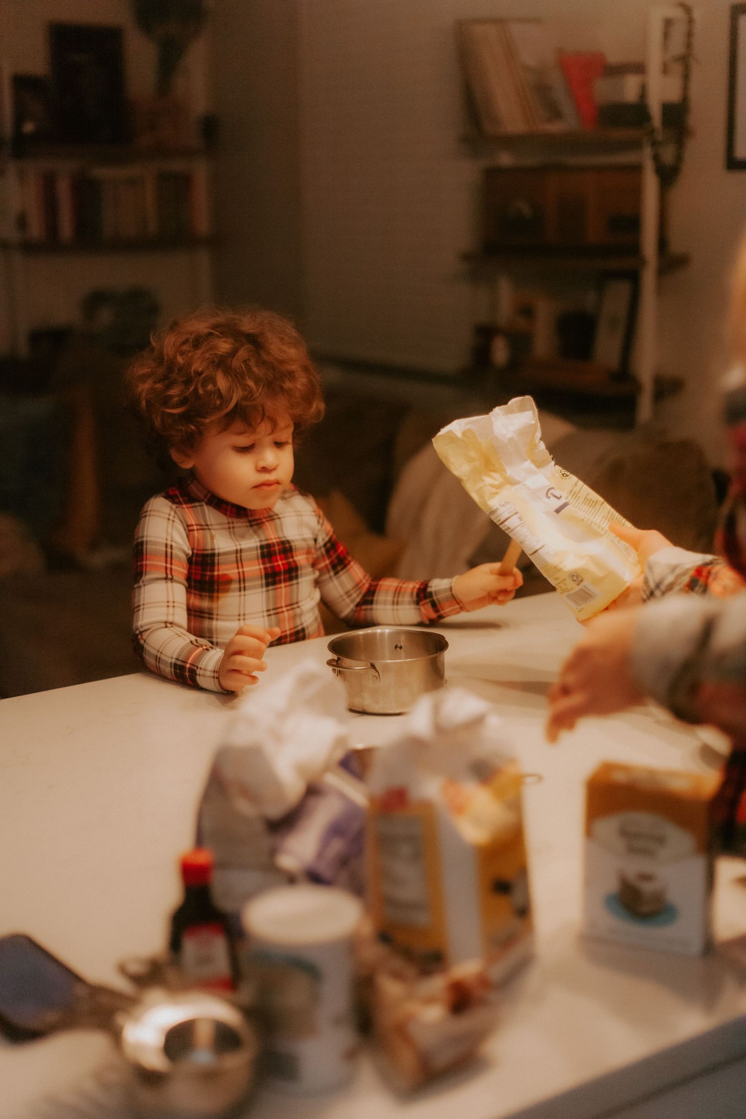 A young child in a plaid shirt helping with baking ingredients at a kitchen counter.