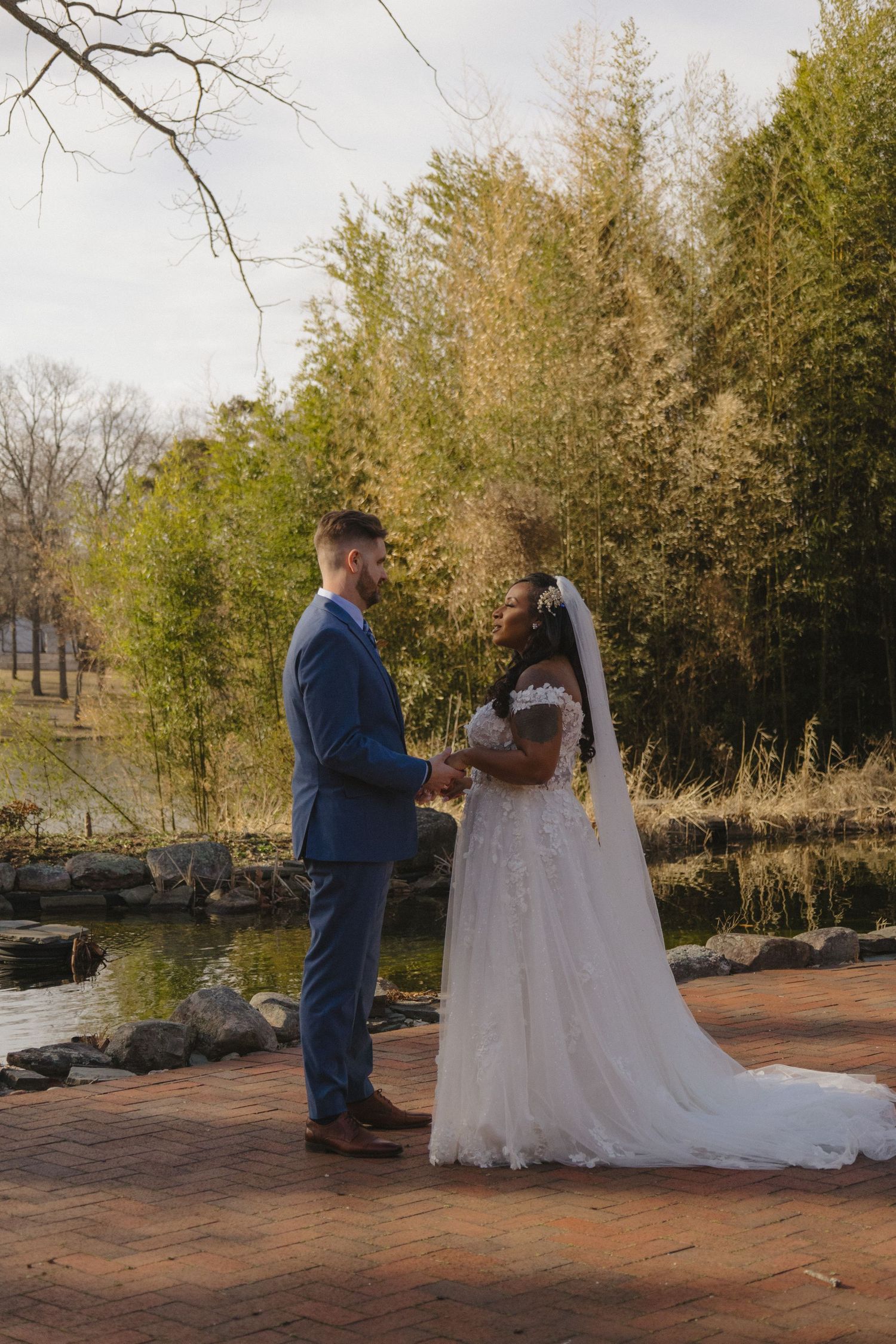 Bride and groom exchanging vows on brick pathway surrounded by winter trees.