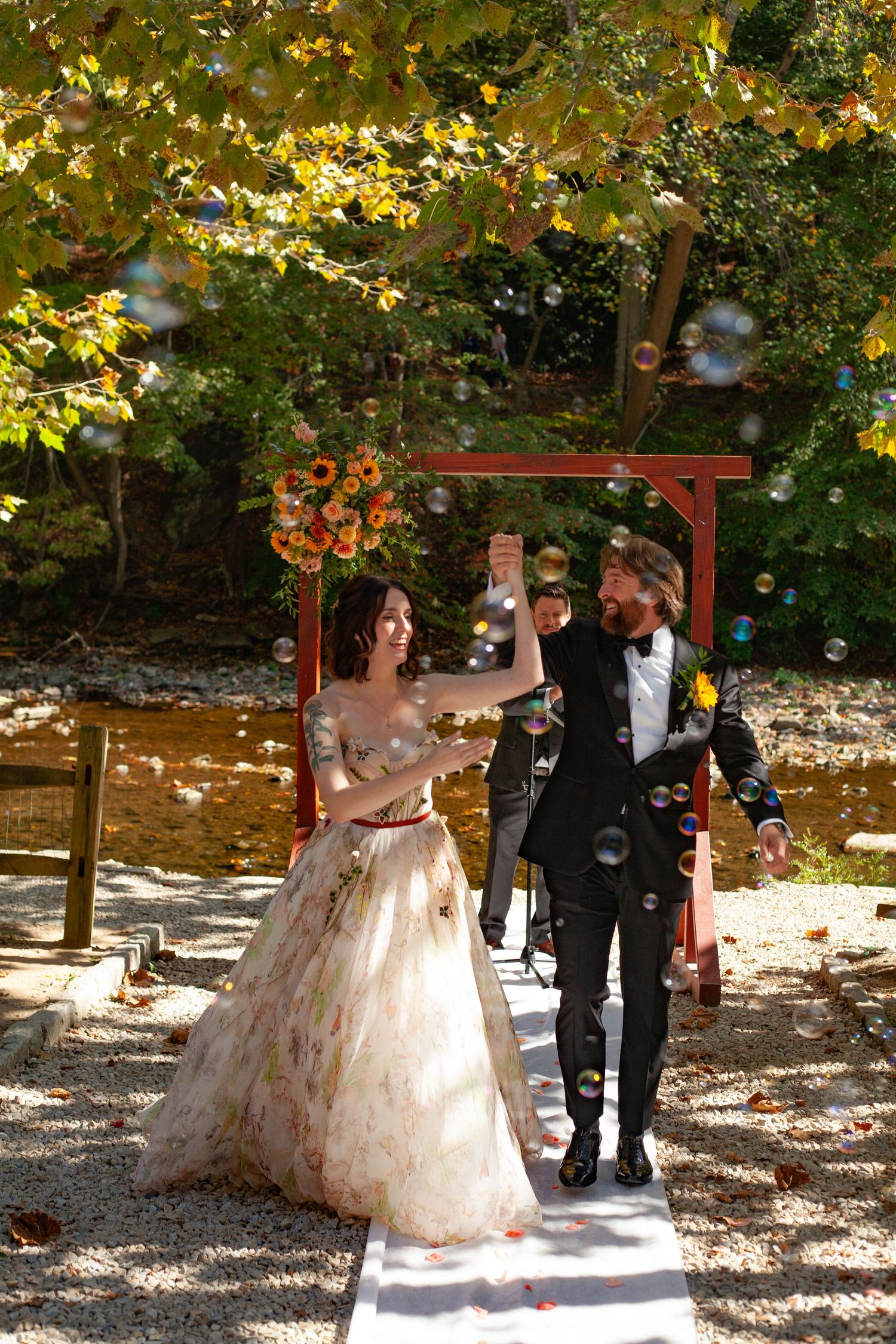 A couple celebrates under falling bubbles in an autumn garden setting.