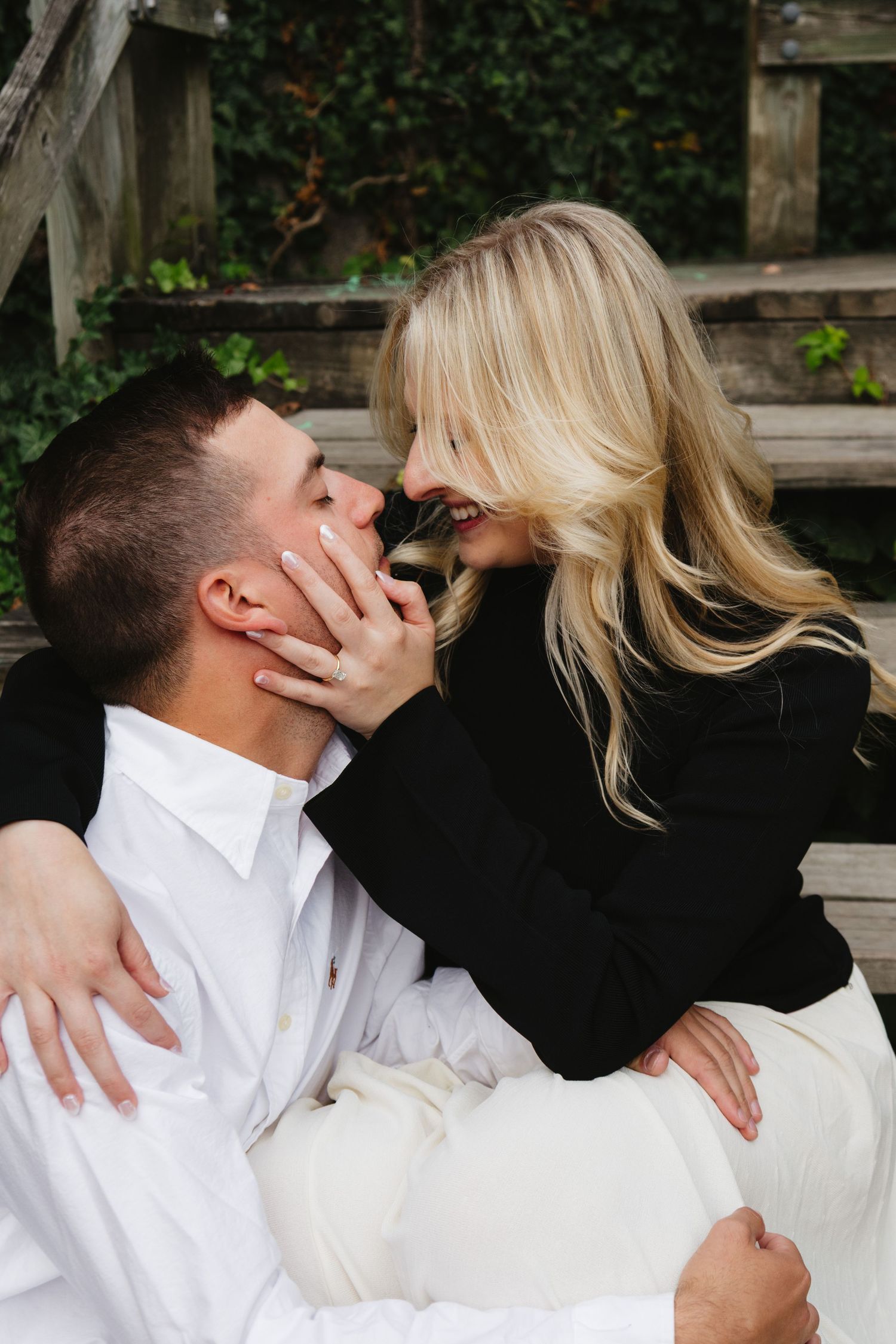 A romantic couple in black and white attire share intimate kisses in an outdoor garden setting.