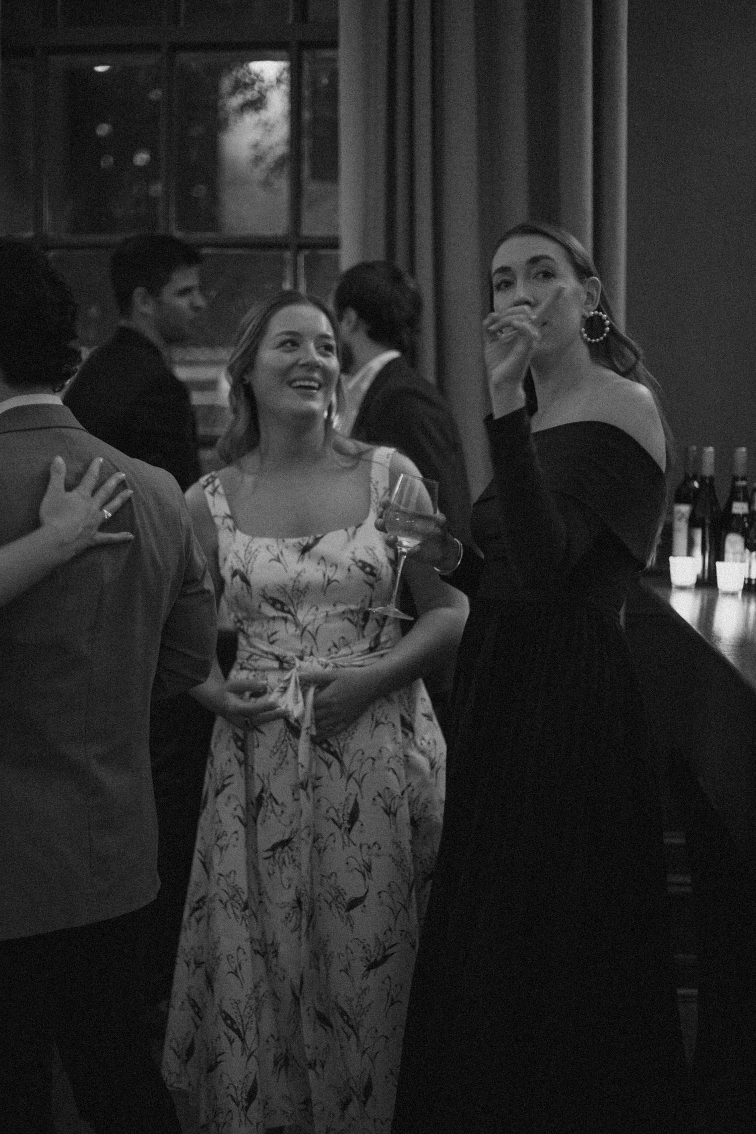 Two people in elegant dresses share a candid moment at an evening event.